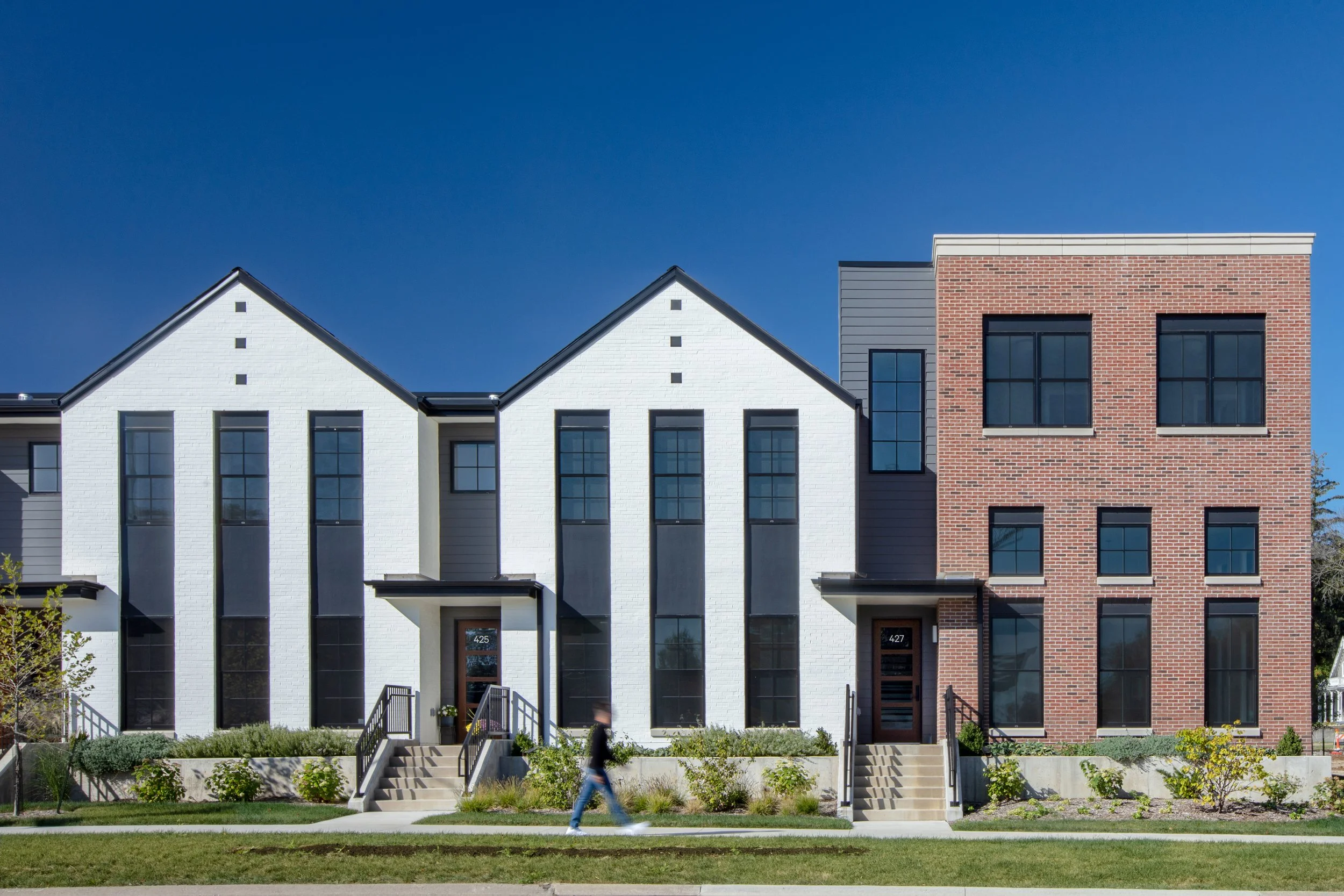 Modern real estate developments by DEV Partners featuring a row of stylish multi-family townhomes, ideal for investing in real estate. Each building showcases distinct white and brick facades with lush landscaping.