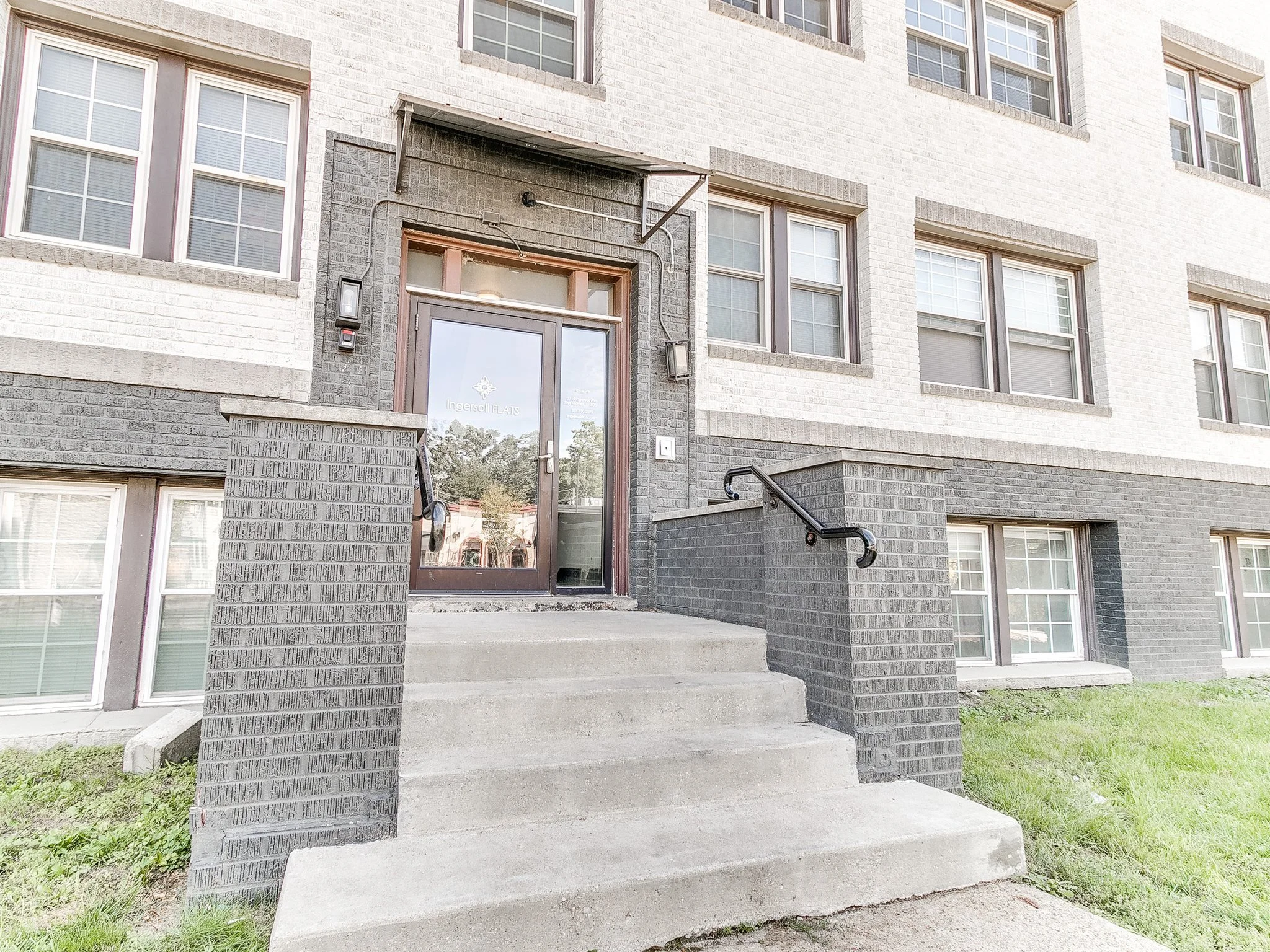 Front entrance of Ingersoll Flats, a multi-family apartment building in Des Moines, Iowa, offering passive income rentals and managed by DEV Partners. The building features a light brick facade with contrasting dark trims and accessible entry.