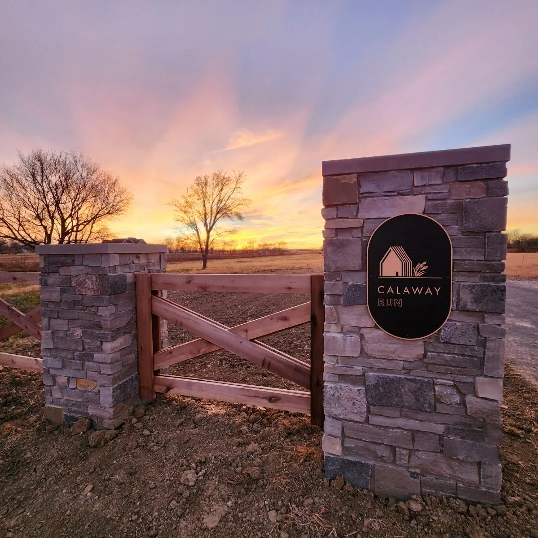 Entrance to Calaway Run in New Albany, Ohio, featuring a stone gate with a wooden fence against a stunning sunset, representing land development opportunities by DEV Partners, ideal for real estate investment.