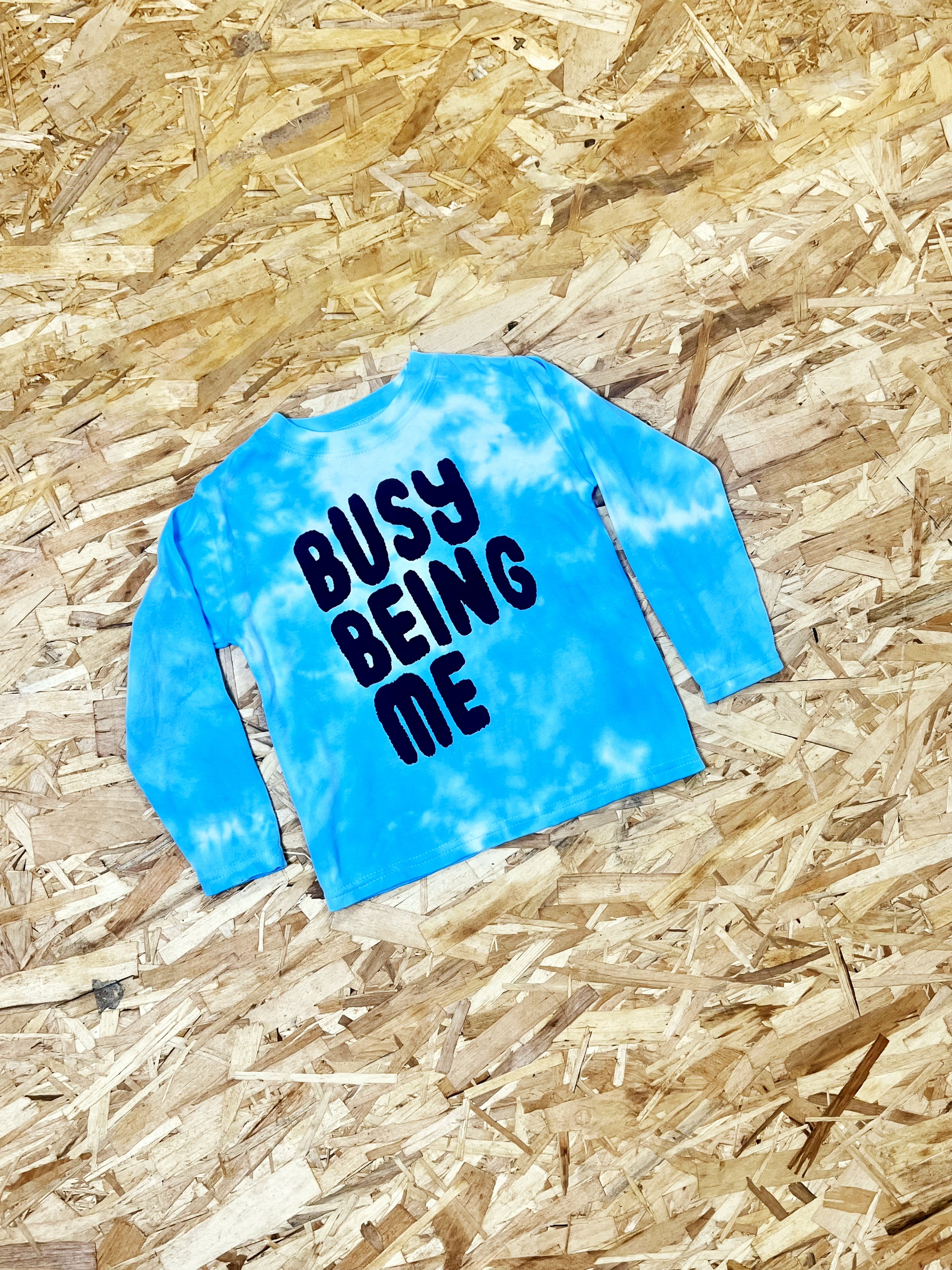 Baby and kids blue tie-dye long-sleeve T-shirt with bold black 'Busy Being Me' typography, celebrating individuality and playful style.