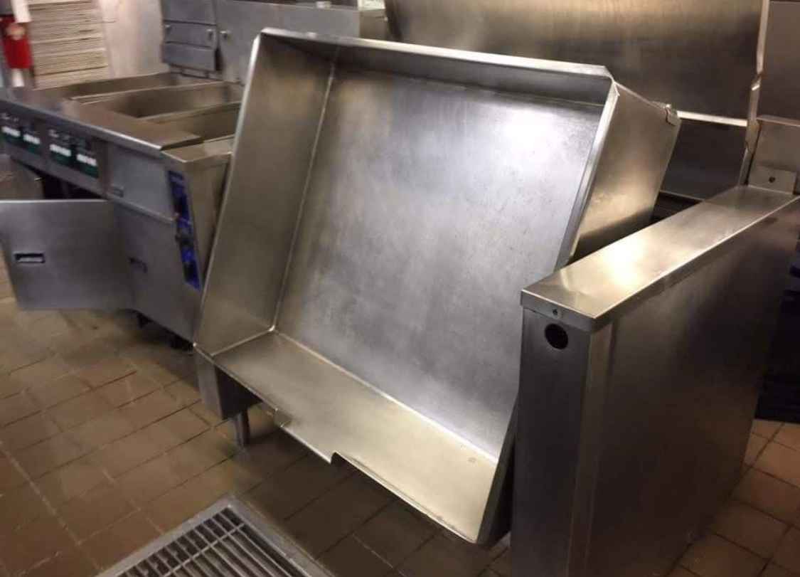 Stainless steel commercial kitchen prep station with a large flat surface and built-in equipment in a restaurant kitchen.