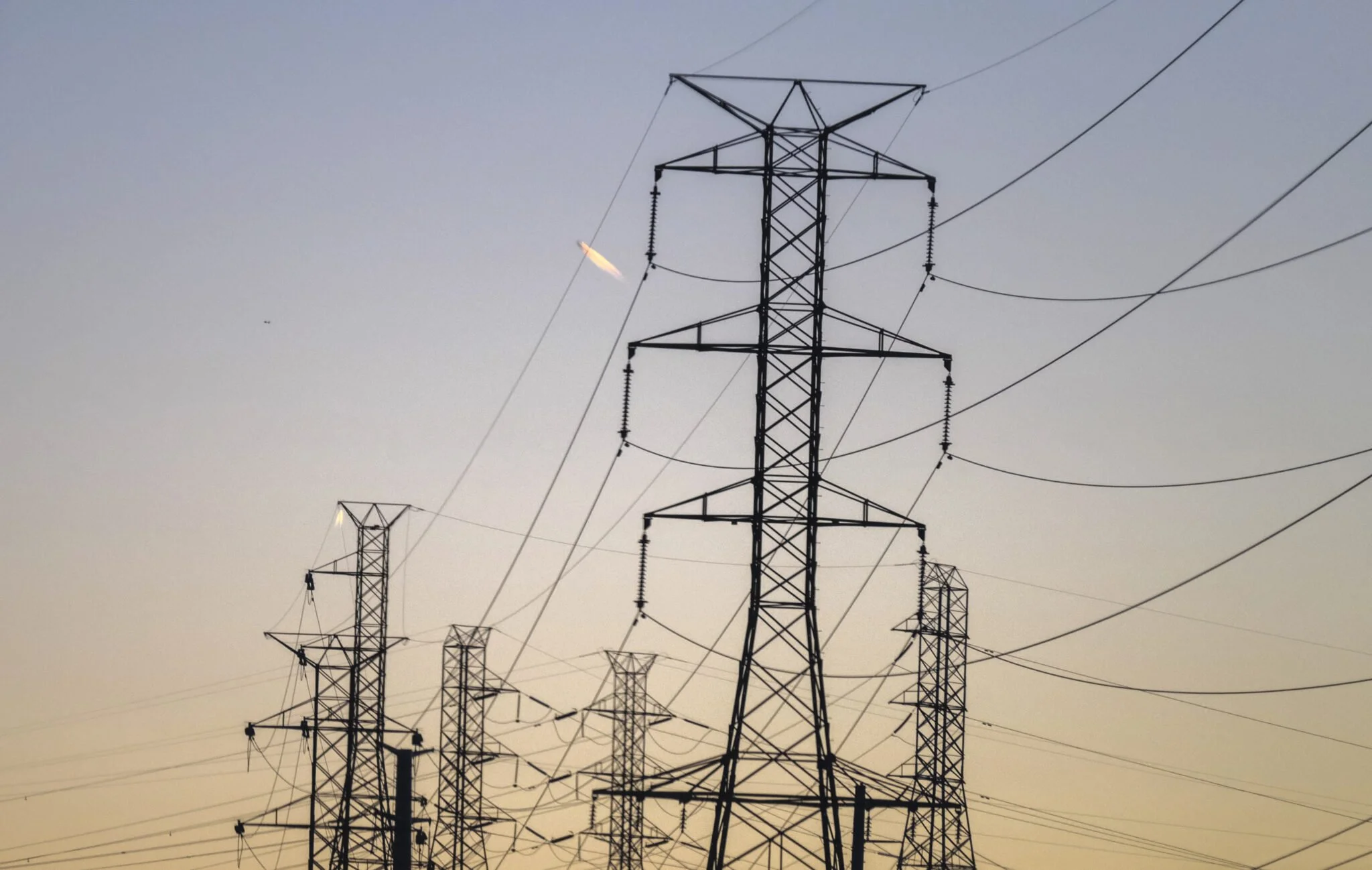 Silhouette of electrical transmission towers with power lines at sunset.