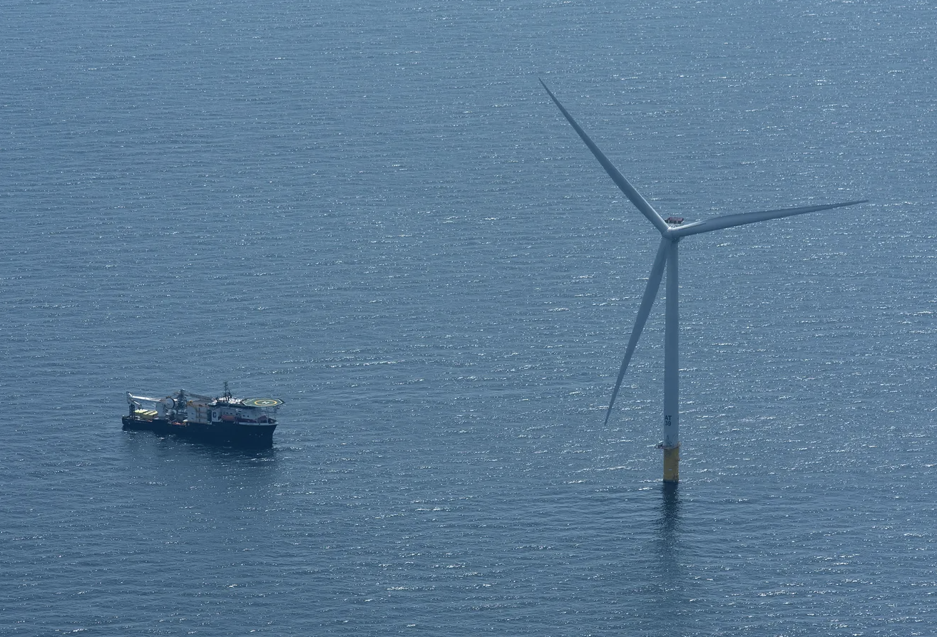 Offshore wind turbine with a service vessel nearby on the ocean.