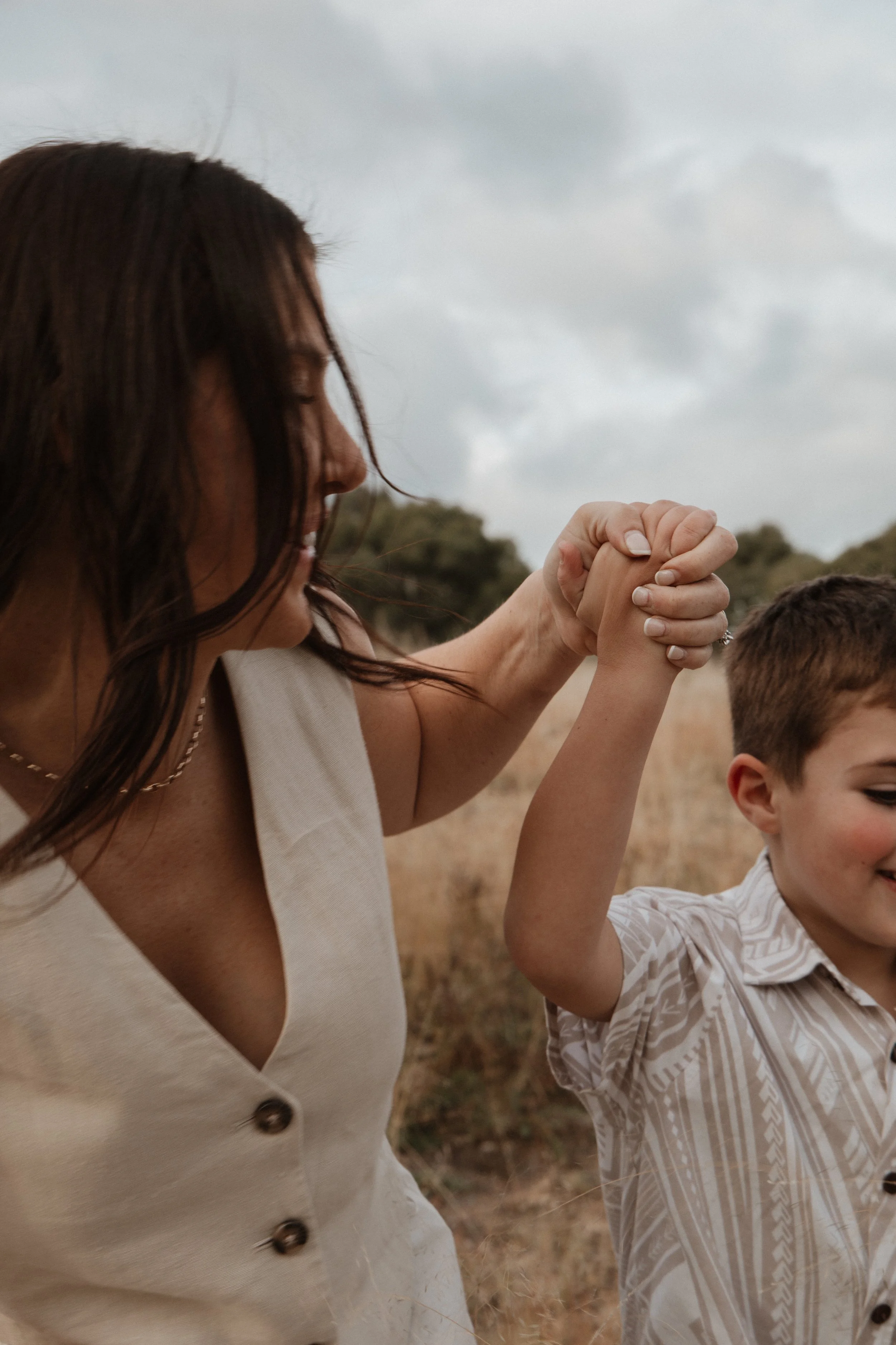 A woman and a child holding hands and smiling outdoors in a field.