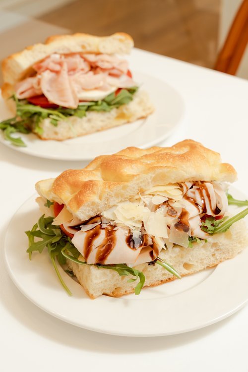 Two gourmet sandwiches with turkey, cheese, arugula, and balsamic glaze on ciabatta bread, served on white plates.