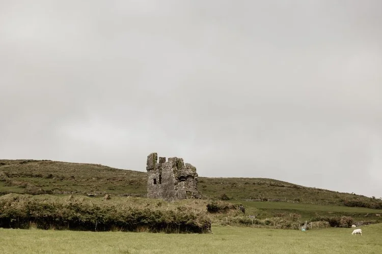 Ruins of an old stone castle on a hillside with green grass, under a cloudy sky - elopement in Ireland venue