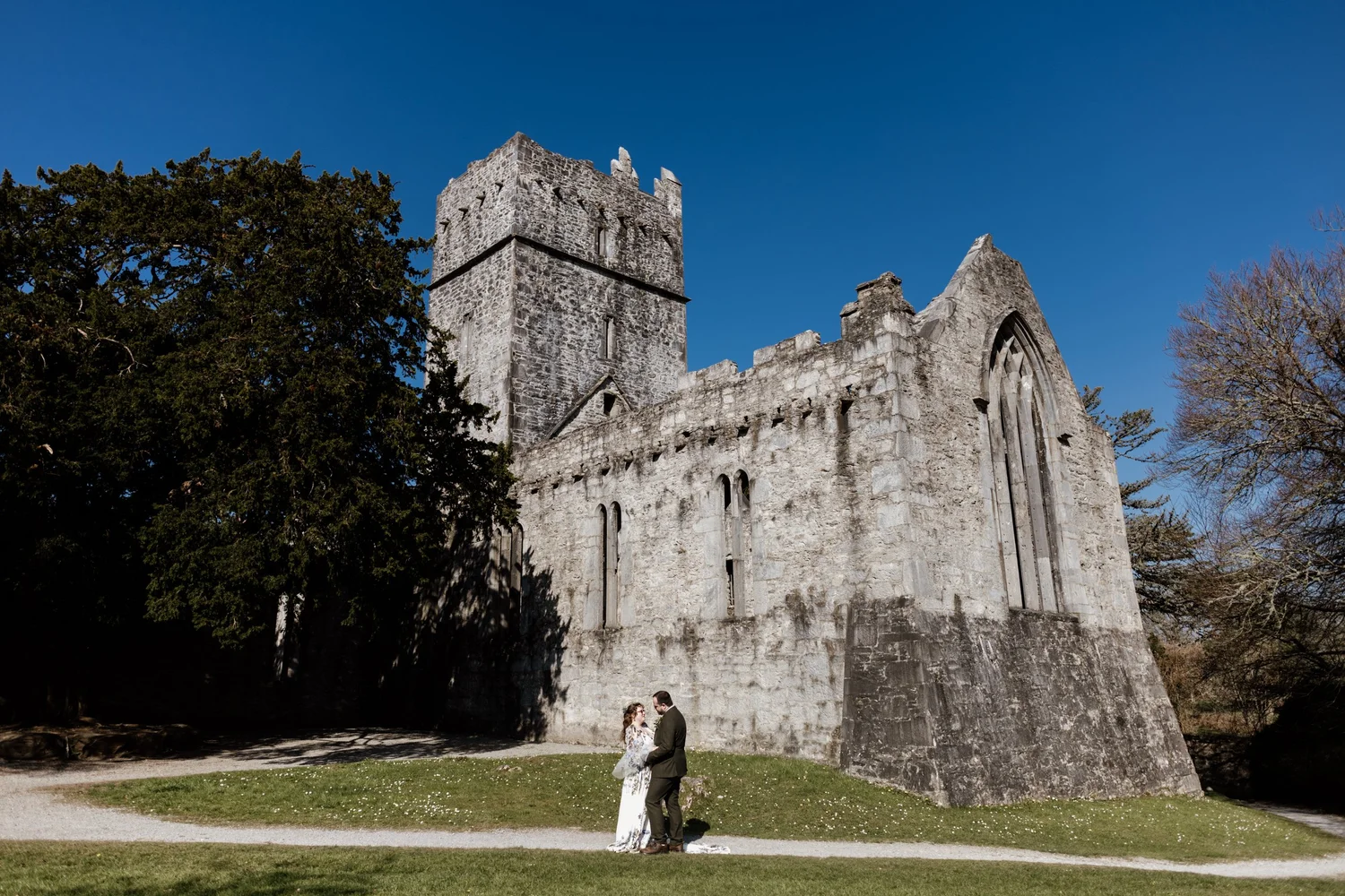 The couple standing in front of the stone abbey under a blue sky