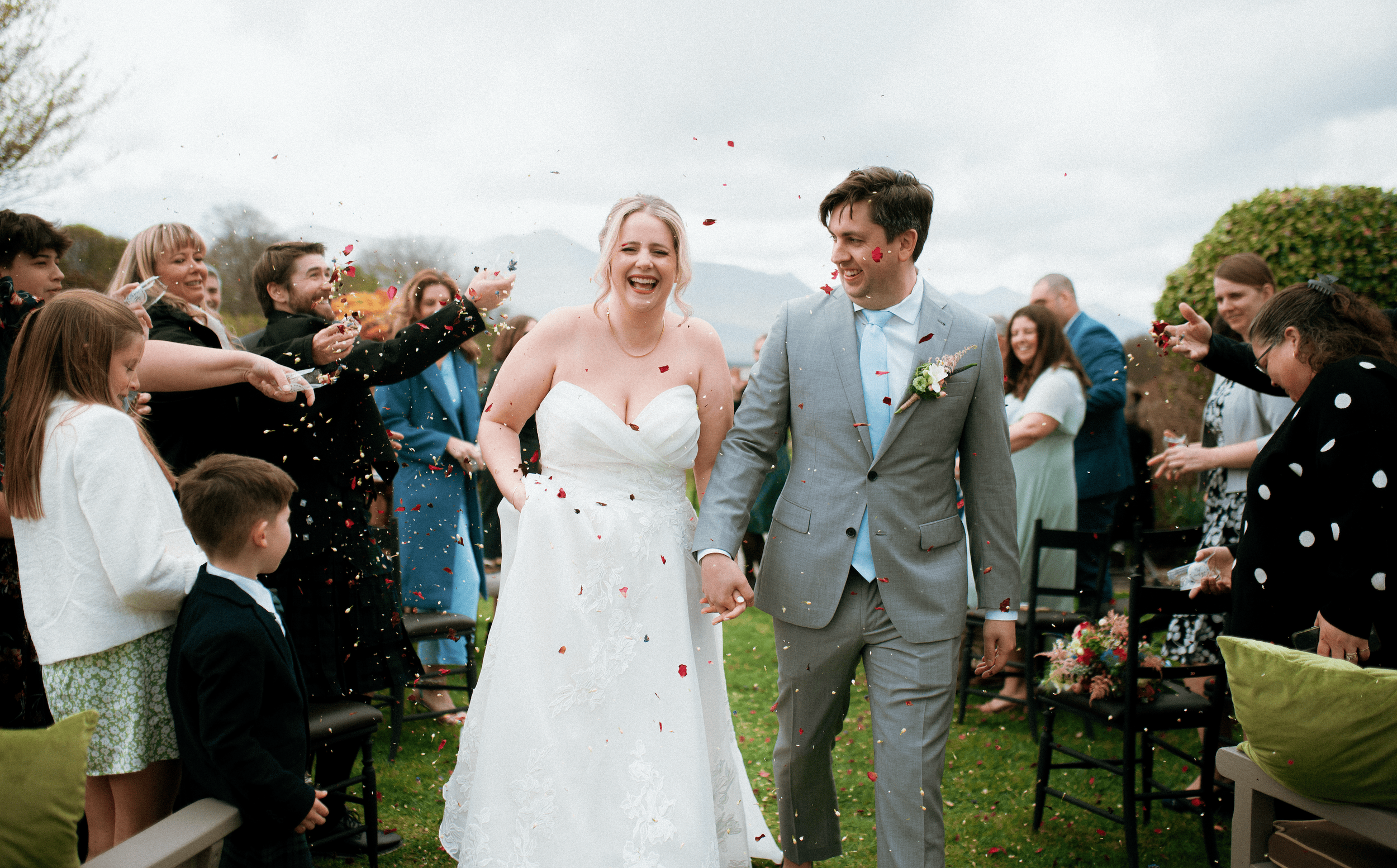 A bride and groom walking hand in hand through a crowd of celebrating guests throwing confetti at an outdoor Ireland wedding