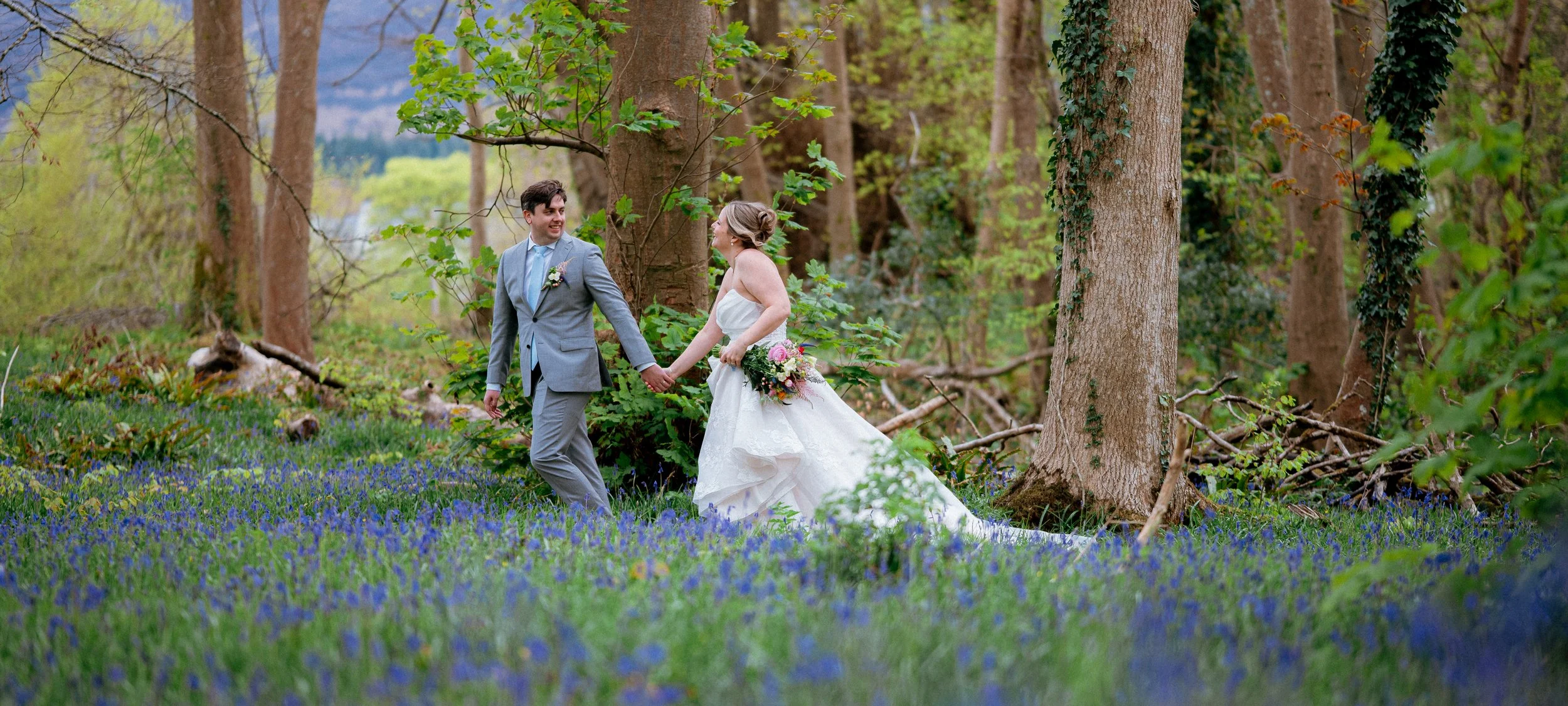 A couple getting married outdoors by a river, with a castle in the background, and an officiant standing behind them.