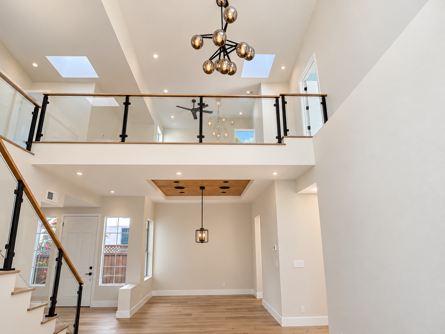 Double-height foyer with a glass railing, skylight, and sculptural chandelier in a contemporary private residence.