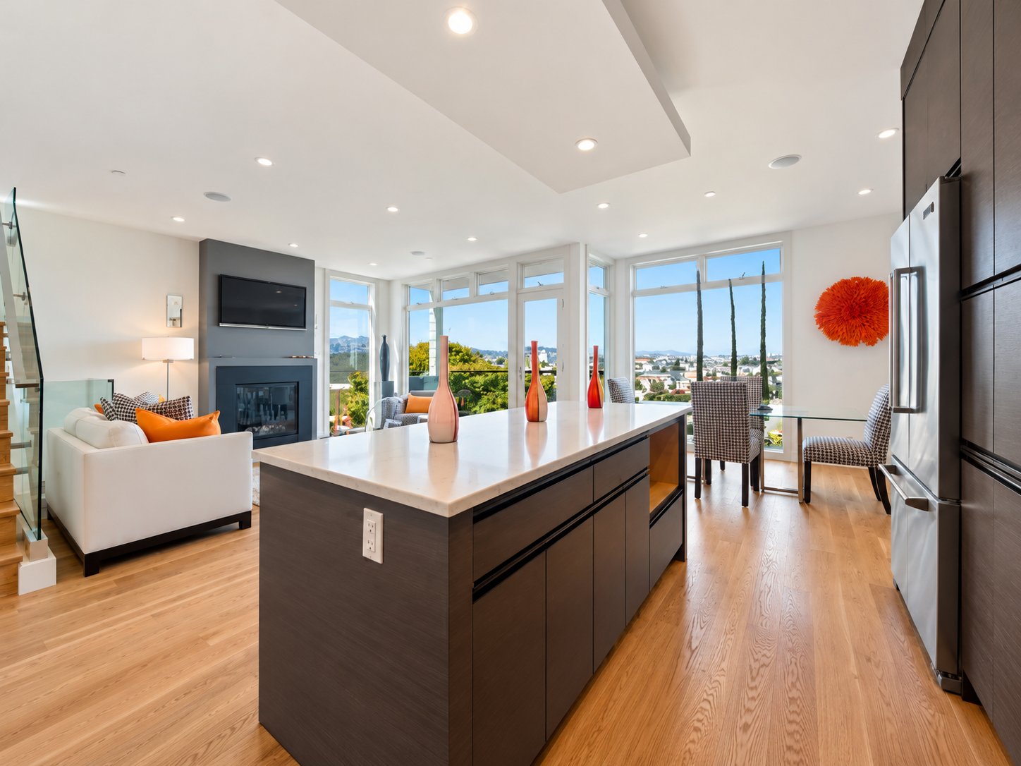 Sunlit kitchen and dining space with an island and floor-to-ceiling windows.