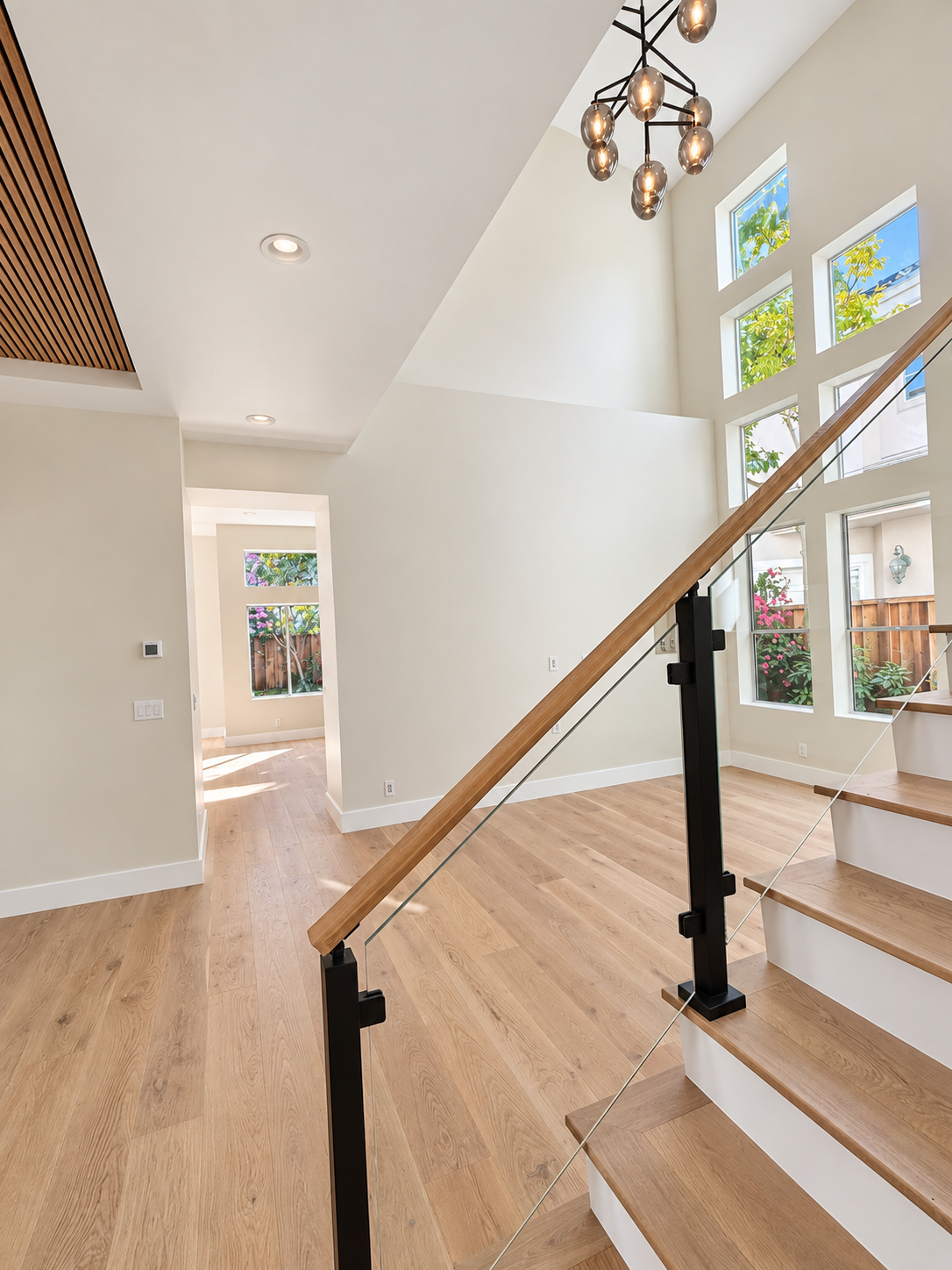 Foyer staircase with wood handrail, glass panels, and tall windows.