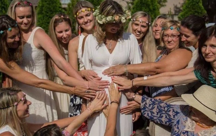 Picture of mom surrounded by love from friends putting their hands on her pregnancy bump.