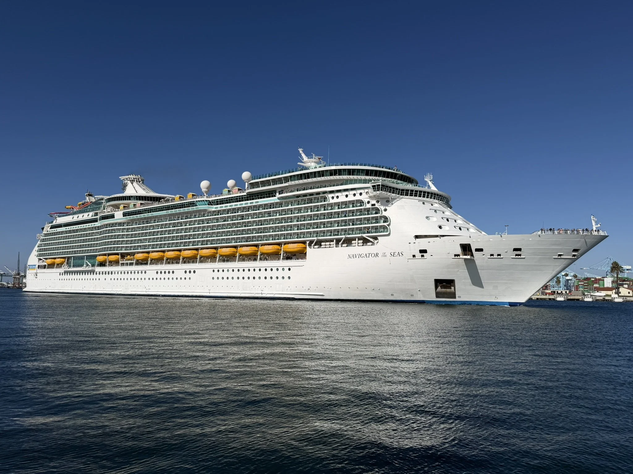 Navigator of the Seas underway in Los Angeles Harbor, with yellow lifeboats beneath rows of balconies.
