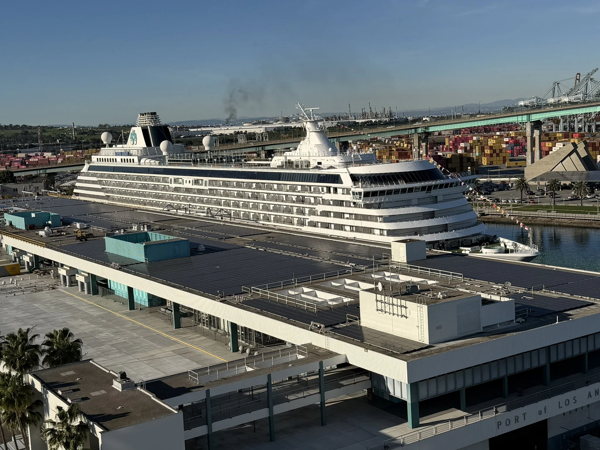 Crystal Serenity docked in Los Angeles, viewed above the cruise terminal with harbor cranes in the distance.