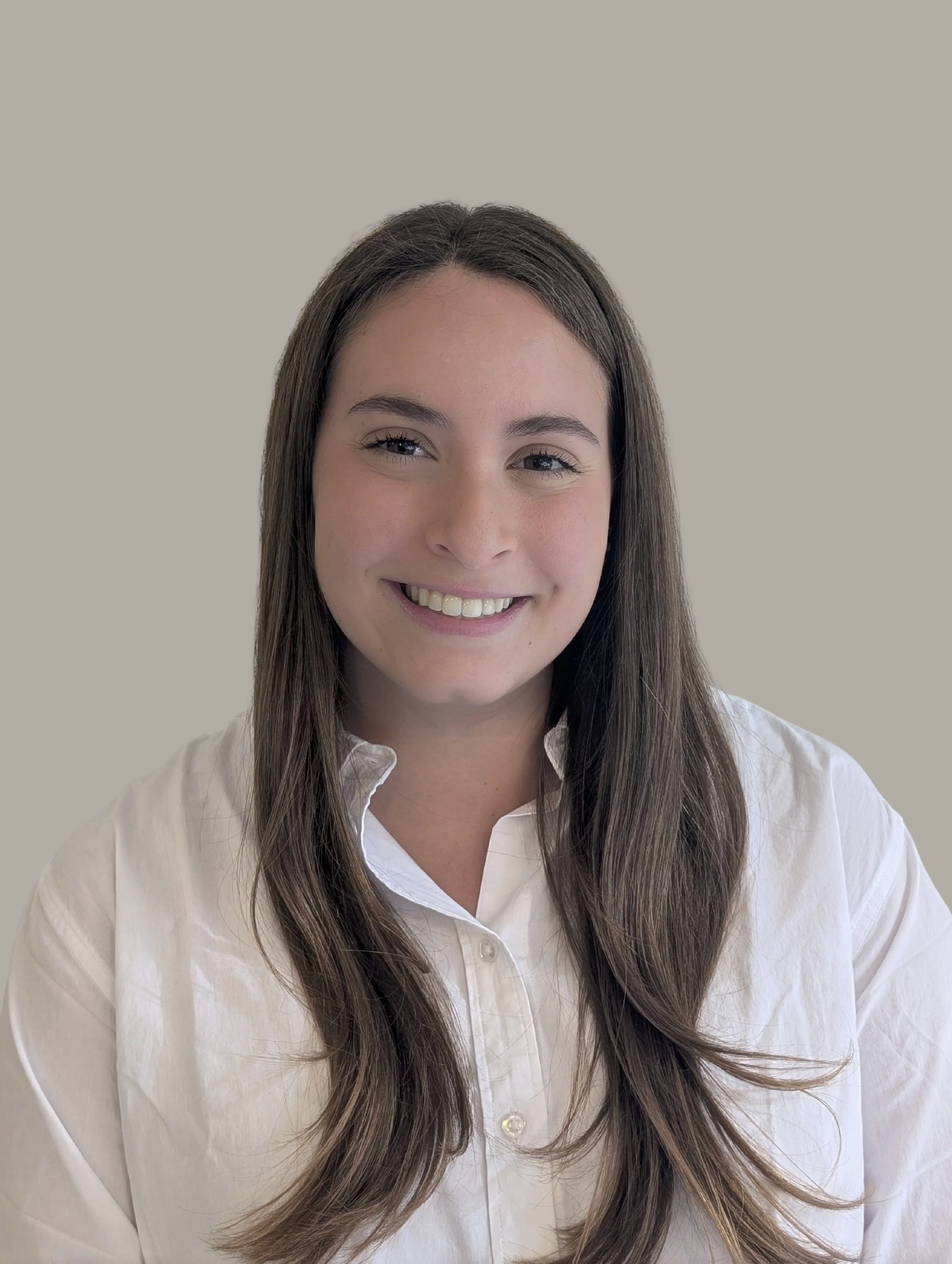 Portrait of a young woman with long brown hair, smiling, wearing a white button-up shirt.