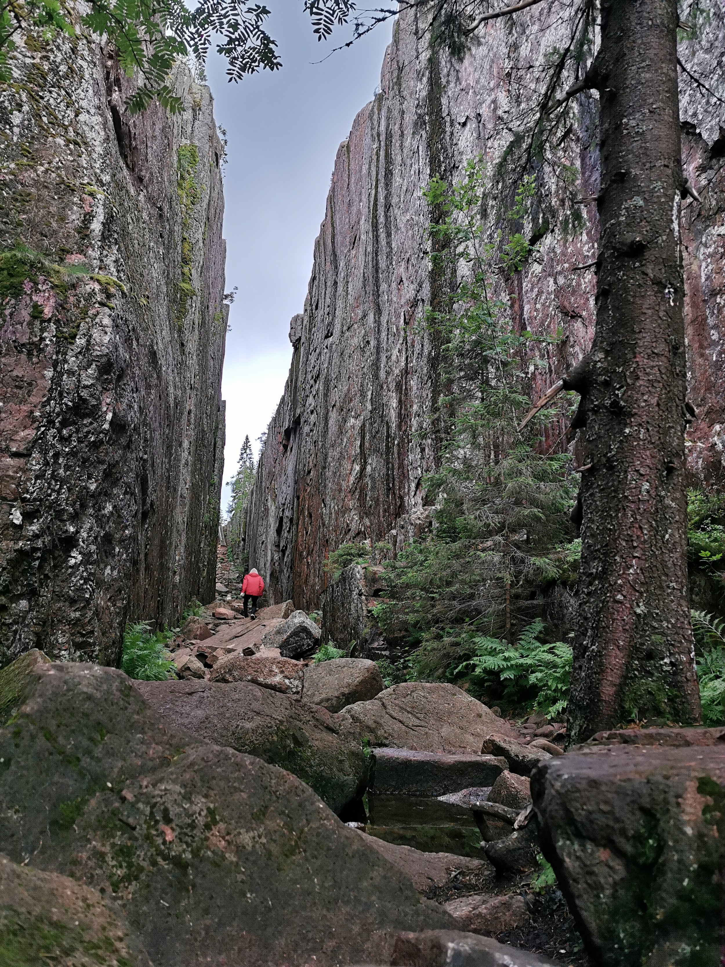 A person hiking through a narrow canyon with tall, rugged rock walls on both sides and a rocky trail leading forward.