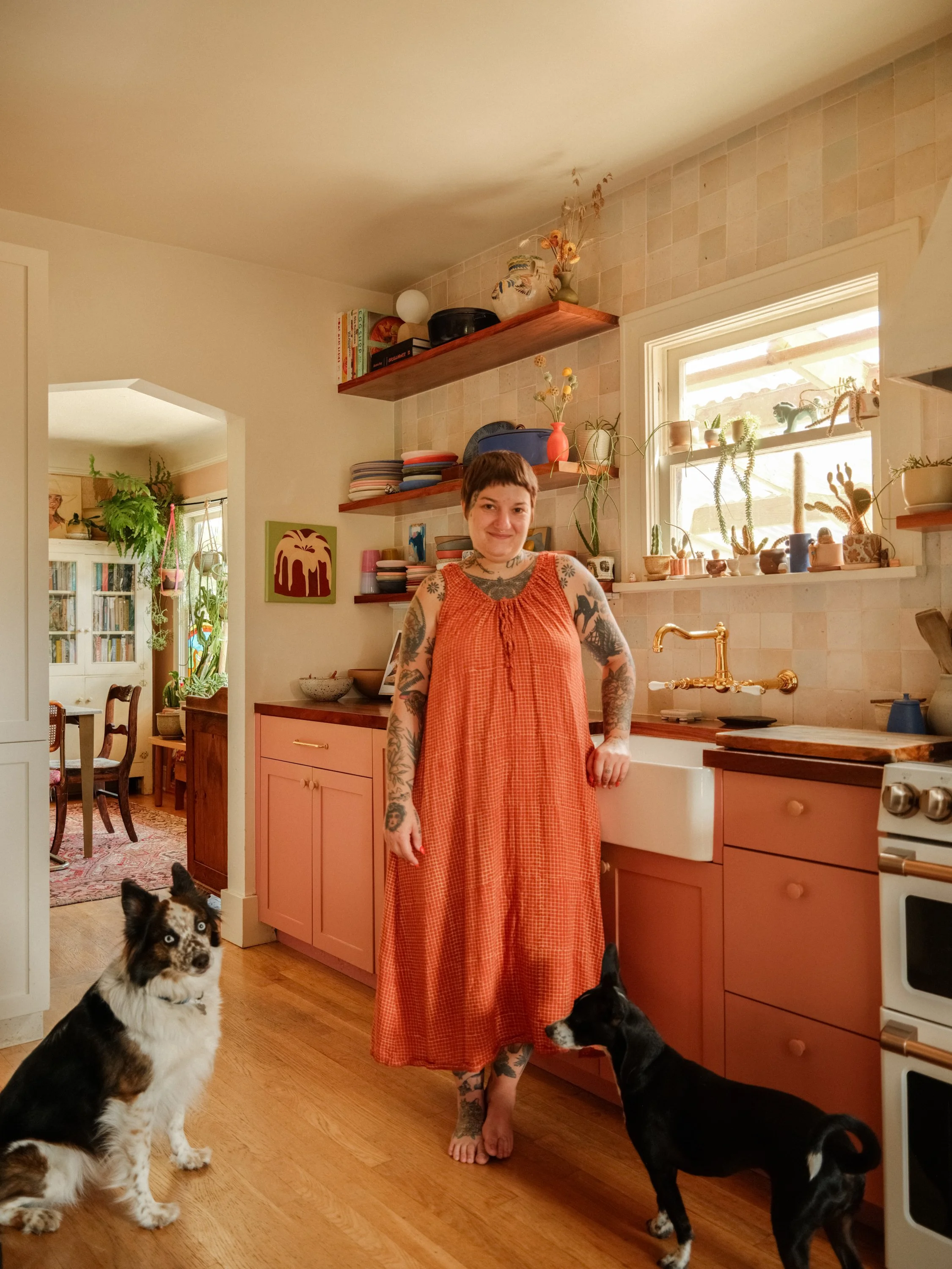 tattooed woman stands in front of a colorful kitchen with her pets