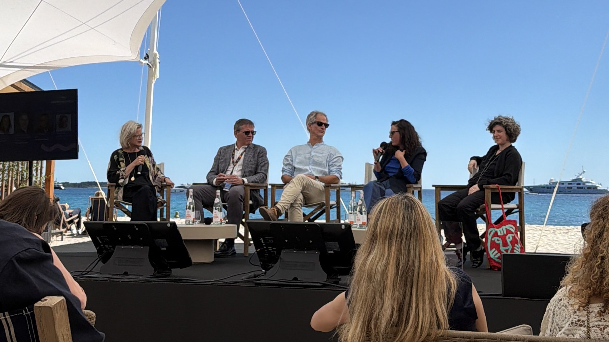 Five panelists seated under a white tent on a beach, speaking about brand investment in film