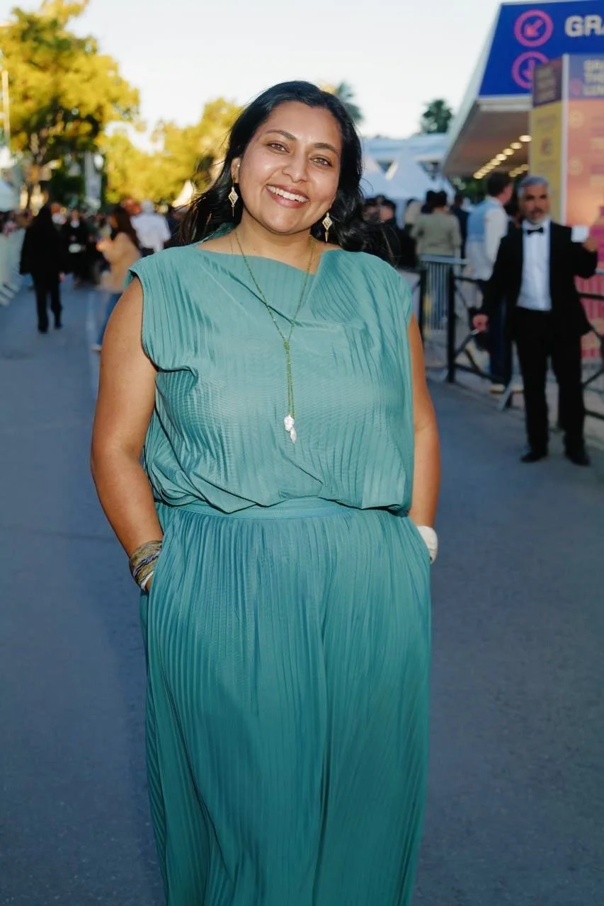 Izzy Abidi smiling at the Cannes Film Festival, wearing a turquoise pleated dress
