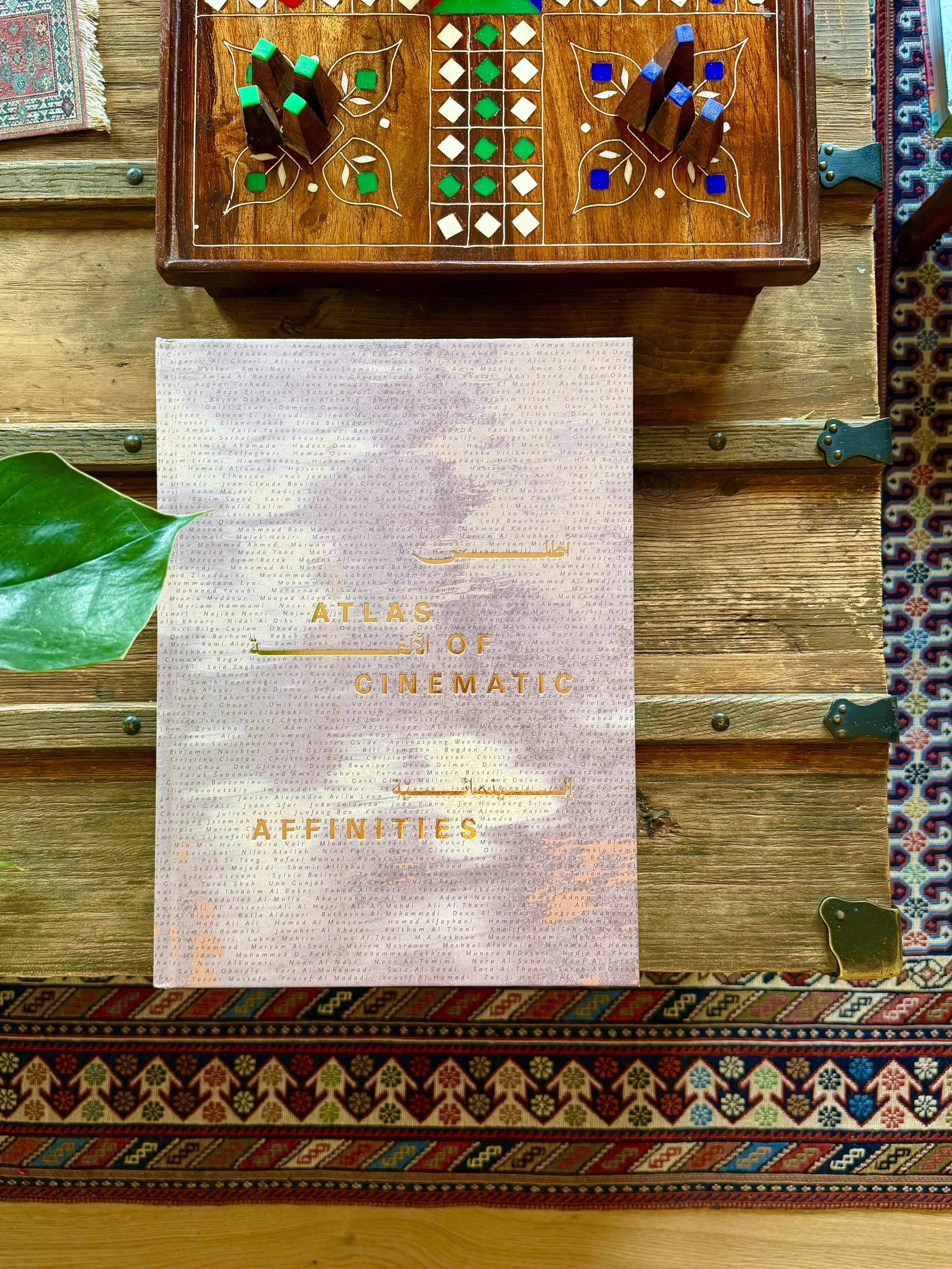 The Atlas of Cinematic Affinities book displayed on a wooden surface with decorative items, showing gold lettering and bilingual Arabic-English text