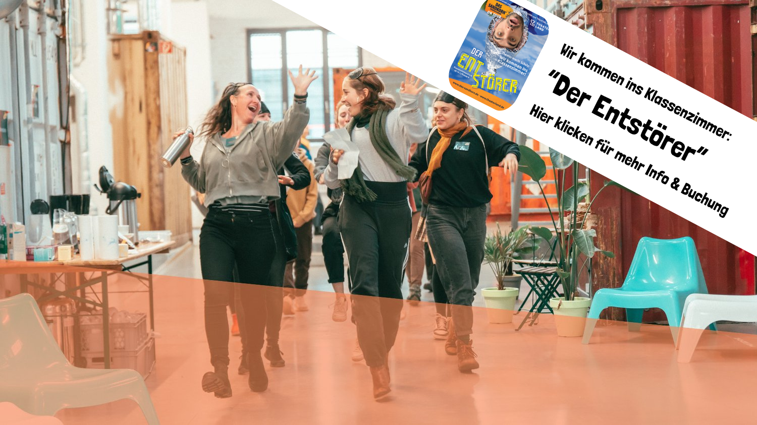 Junge Frauen lachen und gehen lachend durch einen Gemeinschaftsraum mit weißen, blauen und braunen Stühlen, Pflanzen und einem Tisch mit Kaffee und Snacks, begleitet von einem Textbanner auf der rechten Seite, das Werbung für ein Theaterstück namens 'Der Entstörer' macht.