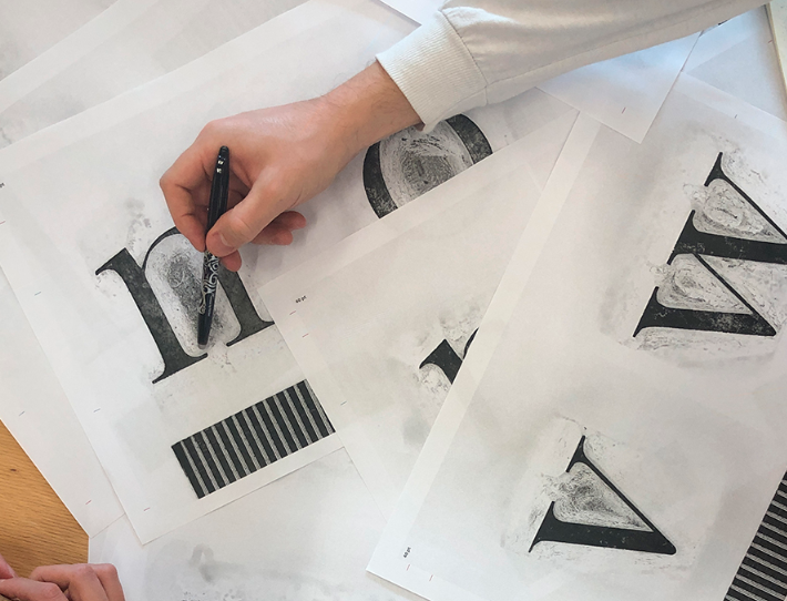 photography showing designer's hand, pen and drawings of letterforms