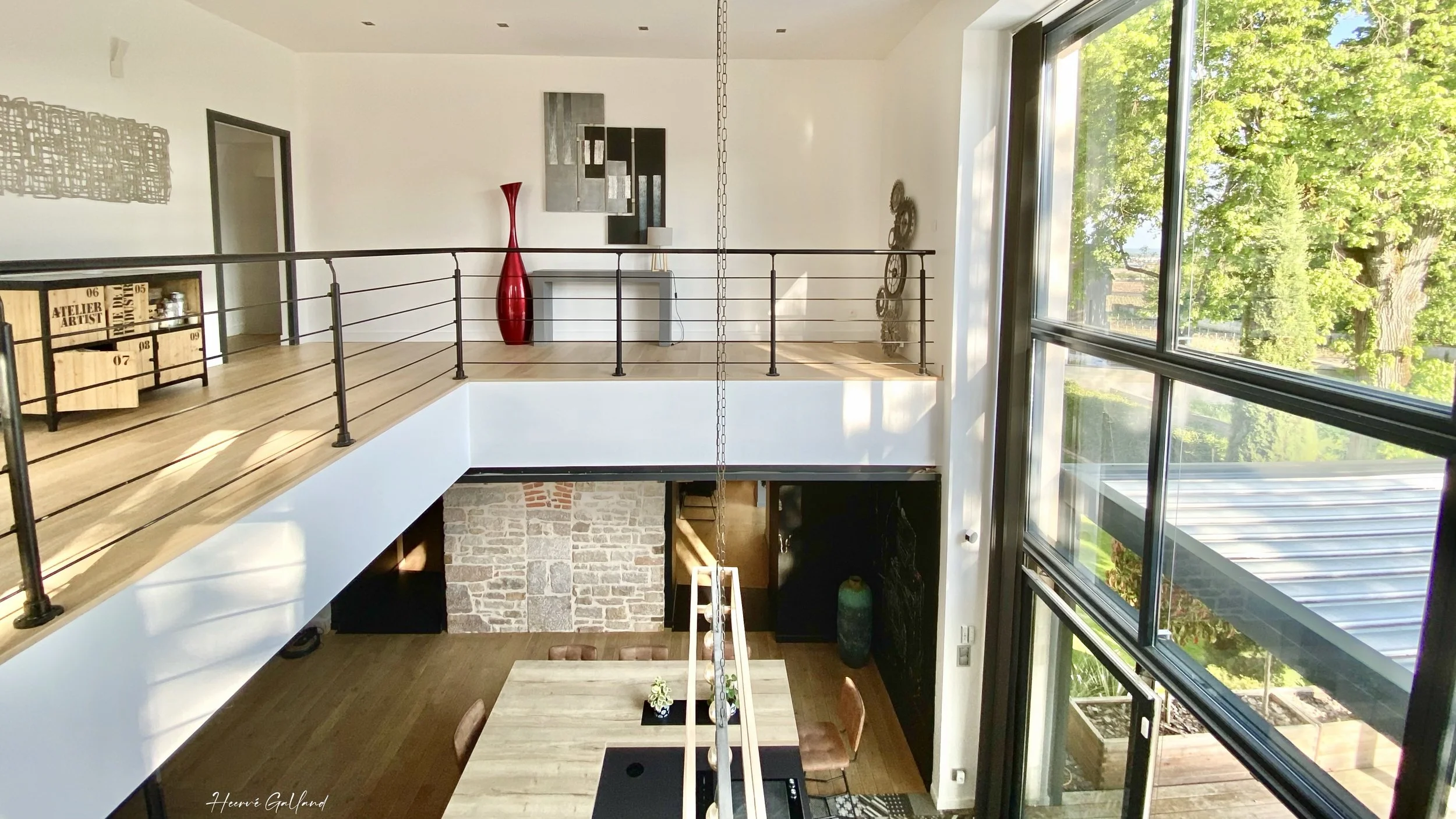 Intérieur d'une maison moderne avec un espace salle à manger au rez-de-chaussée et un mezzanine au premier étage, grande fenêtre laissant entrer de la lumière naturelle.