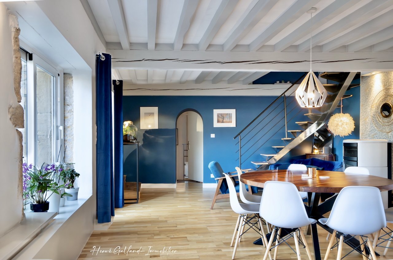 Salle à manger avec table en bois, chaises blanches, mur bleu, escalier en métal, lampe design