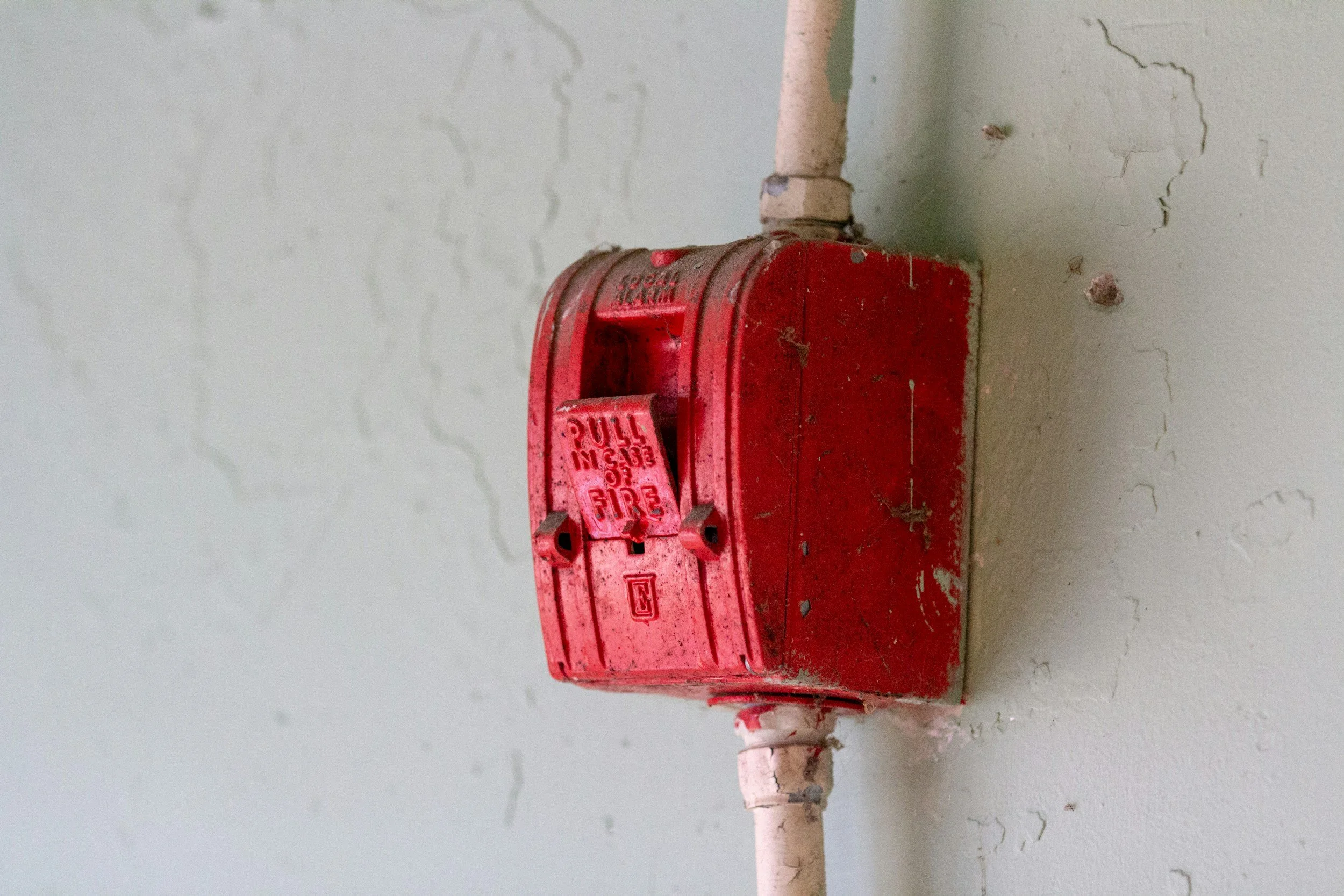 Red fire alarm box mounted on a wall with peeling paint and cracks