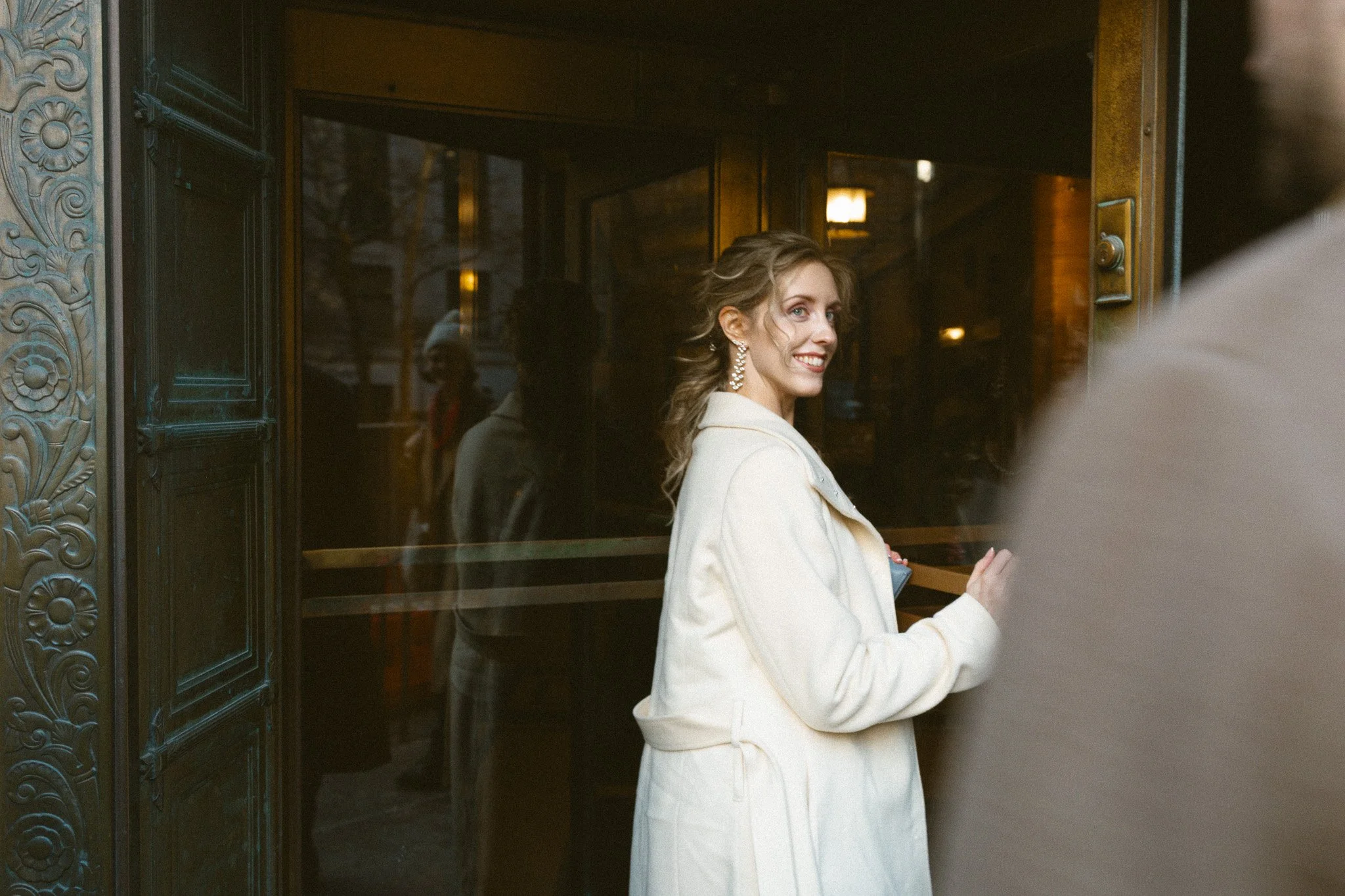 A woman in a white coat smiling at an elevator door.