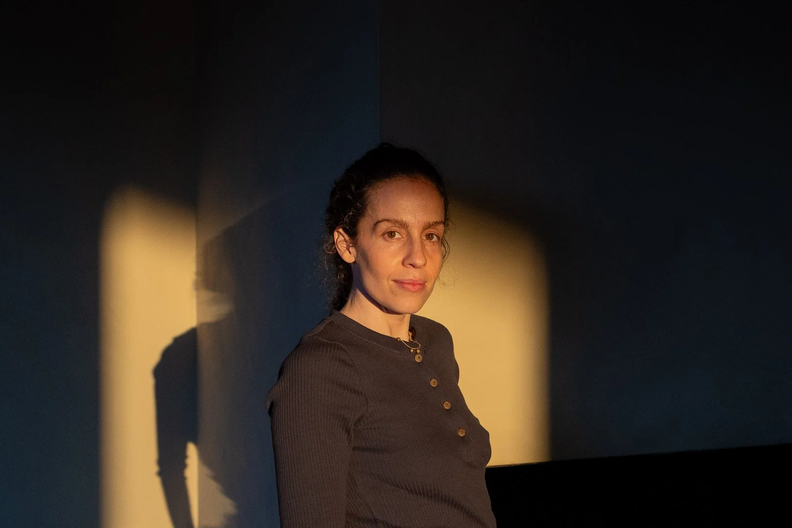 A woman with dark hair and fair skin shining in warm, yellow lighting against a dark background.