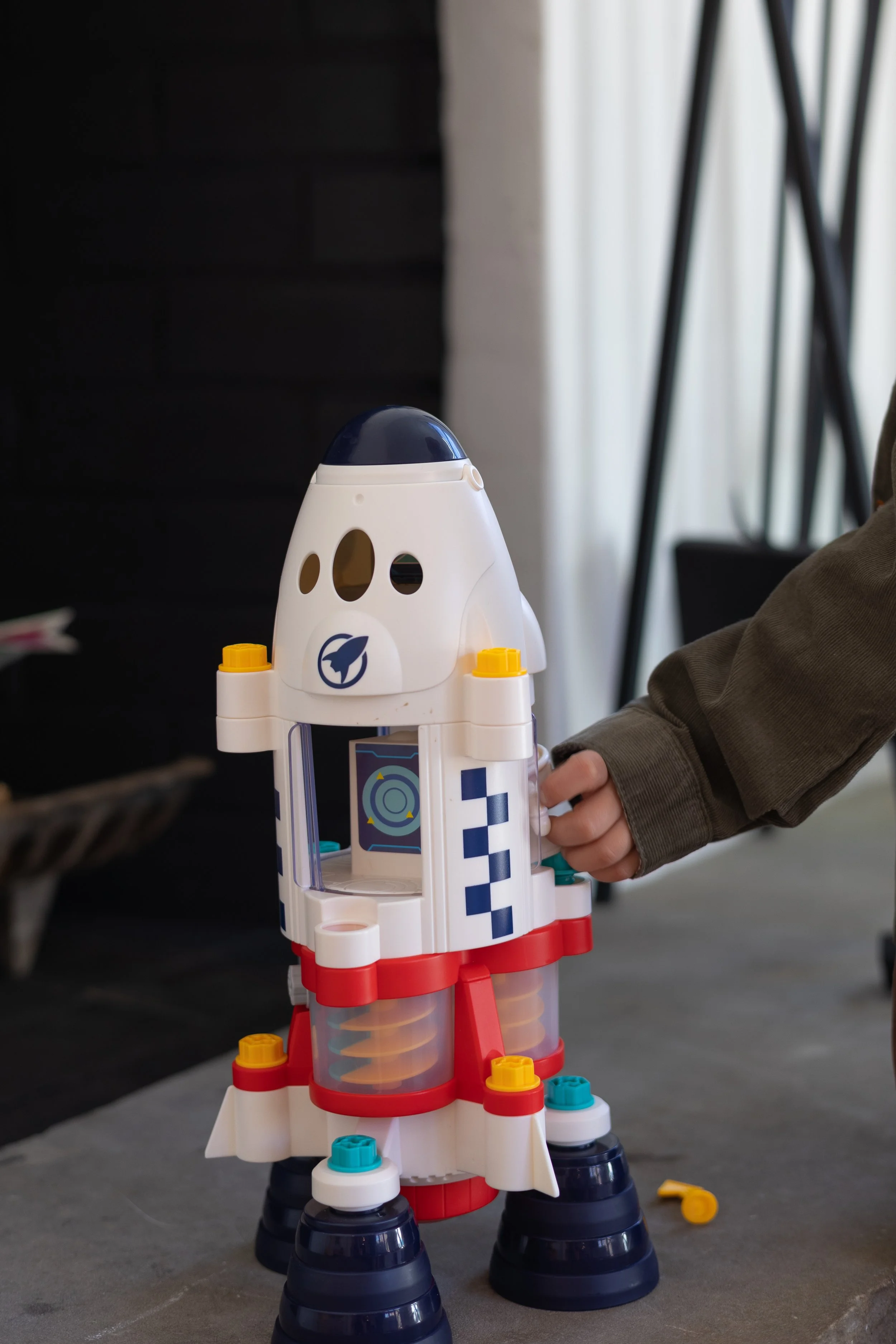 A child's hand holding a toy rocket with a white body, blue and red accents, and black detachable legs on a gray surface.