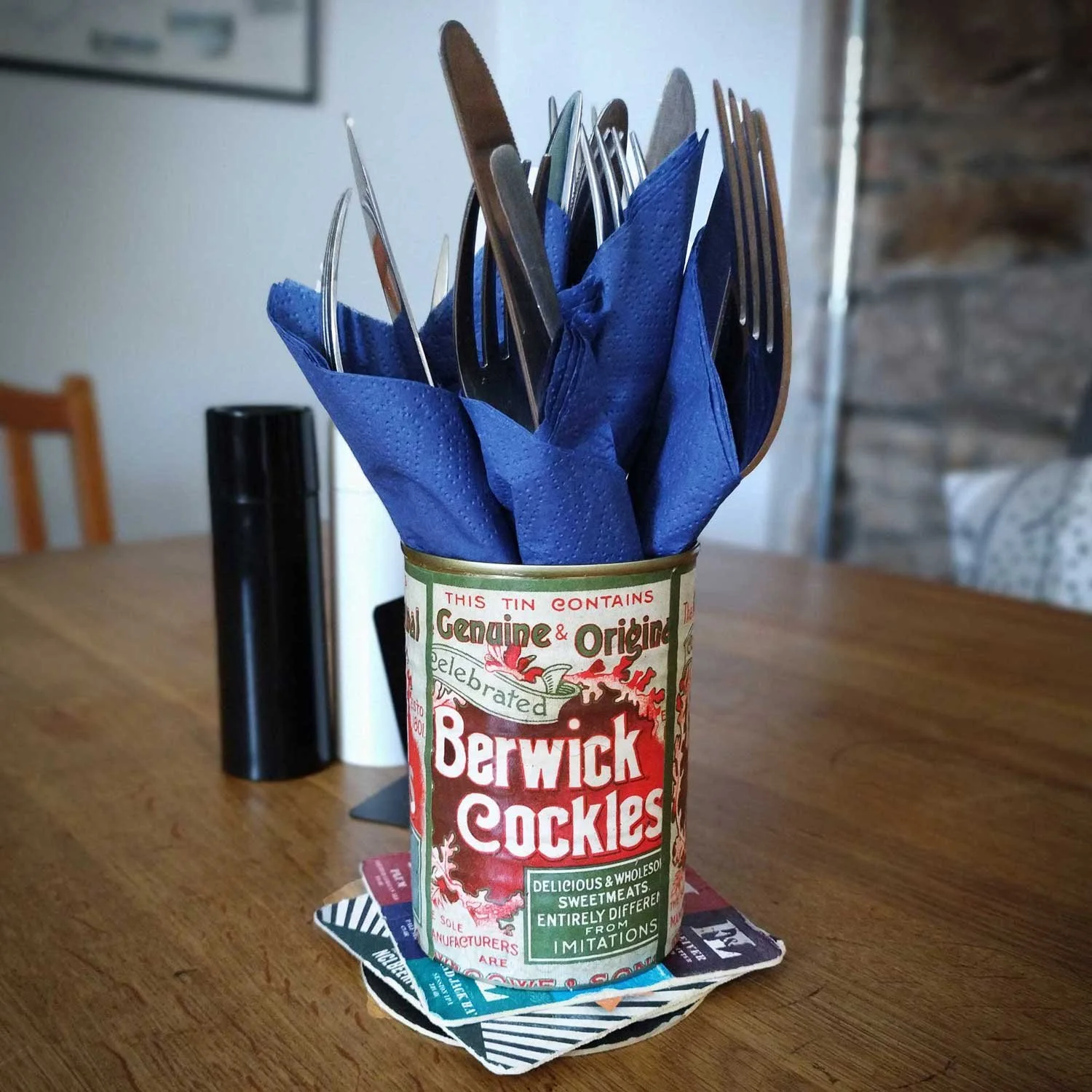 Vintage Berwick Cockles tin used as a cutlery holder on wooden table