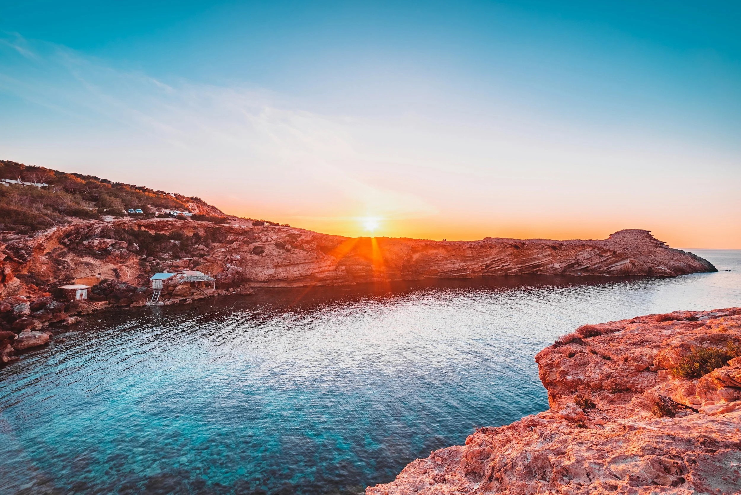 Sunset view over a rocky coastline with clear blue water and cliffs.
