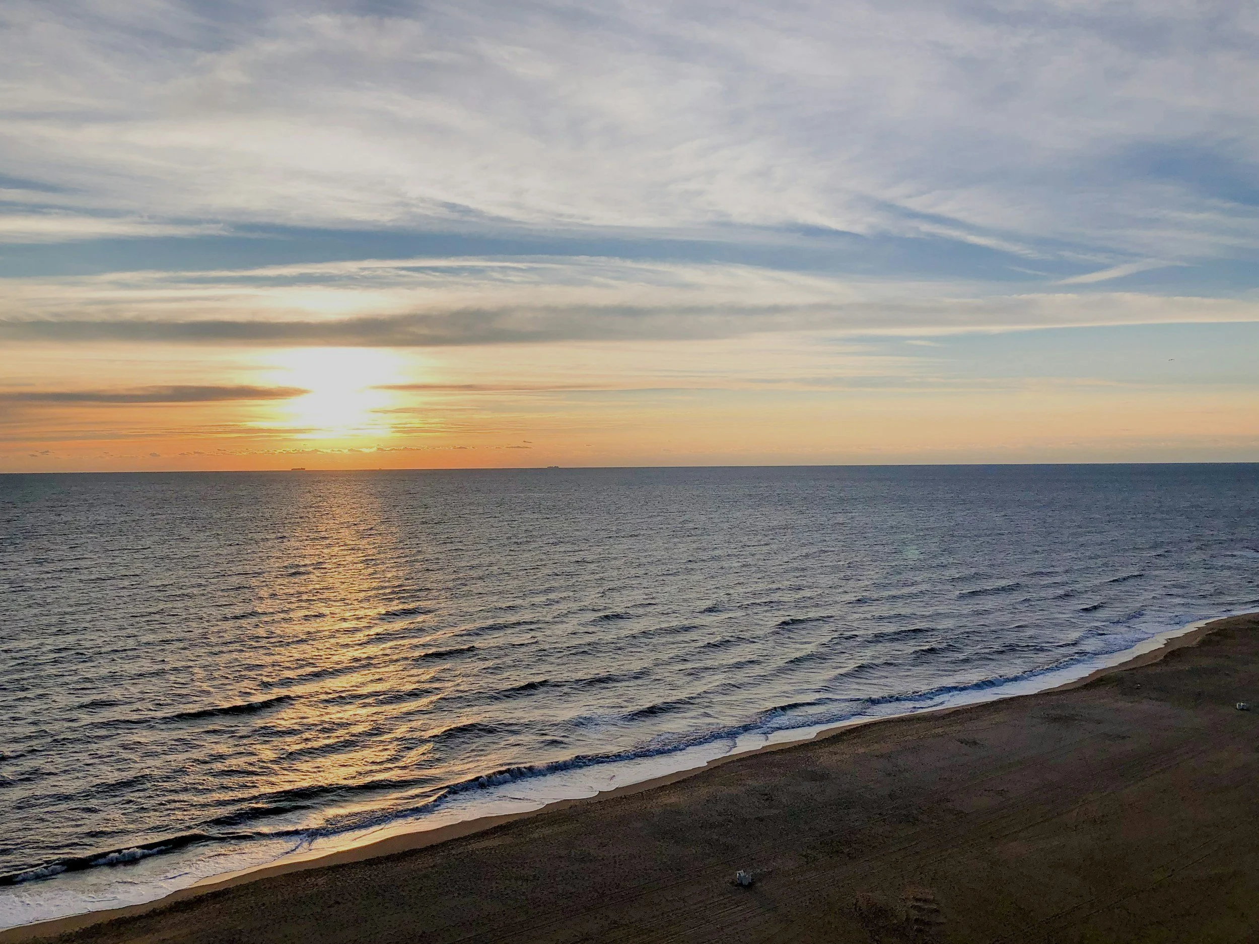 Beach sunrise over ocean with gentle waves and sandy shore