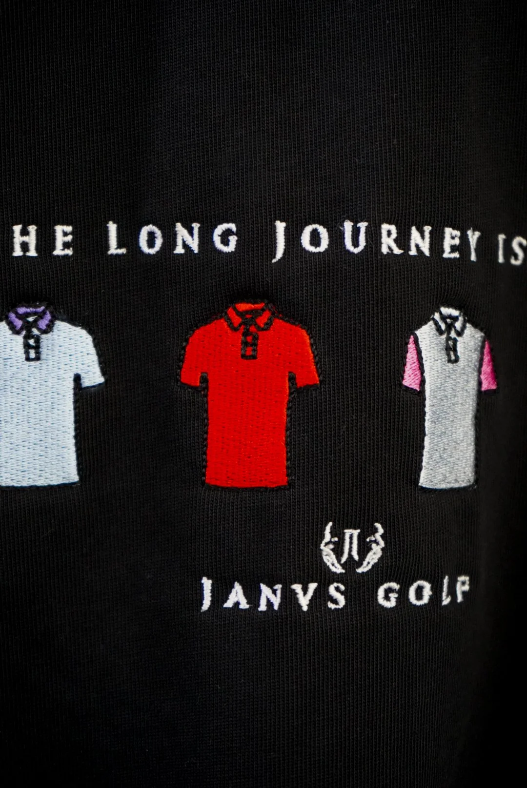 Embroidery of three golf shirts in white, red, and gray with purple, red, and pink sleeves, on black fabric. Text reads 'The Long Journey' above the shirts and 'JANS GOLF' below the shirts.