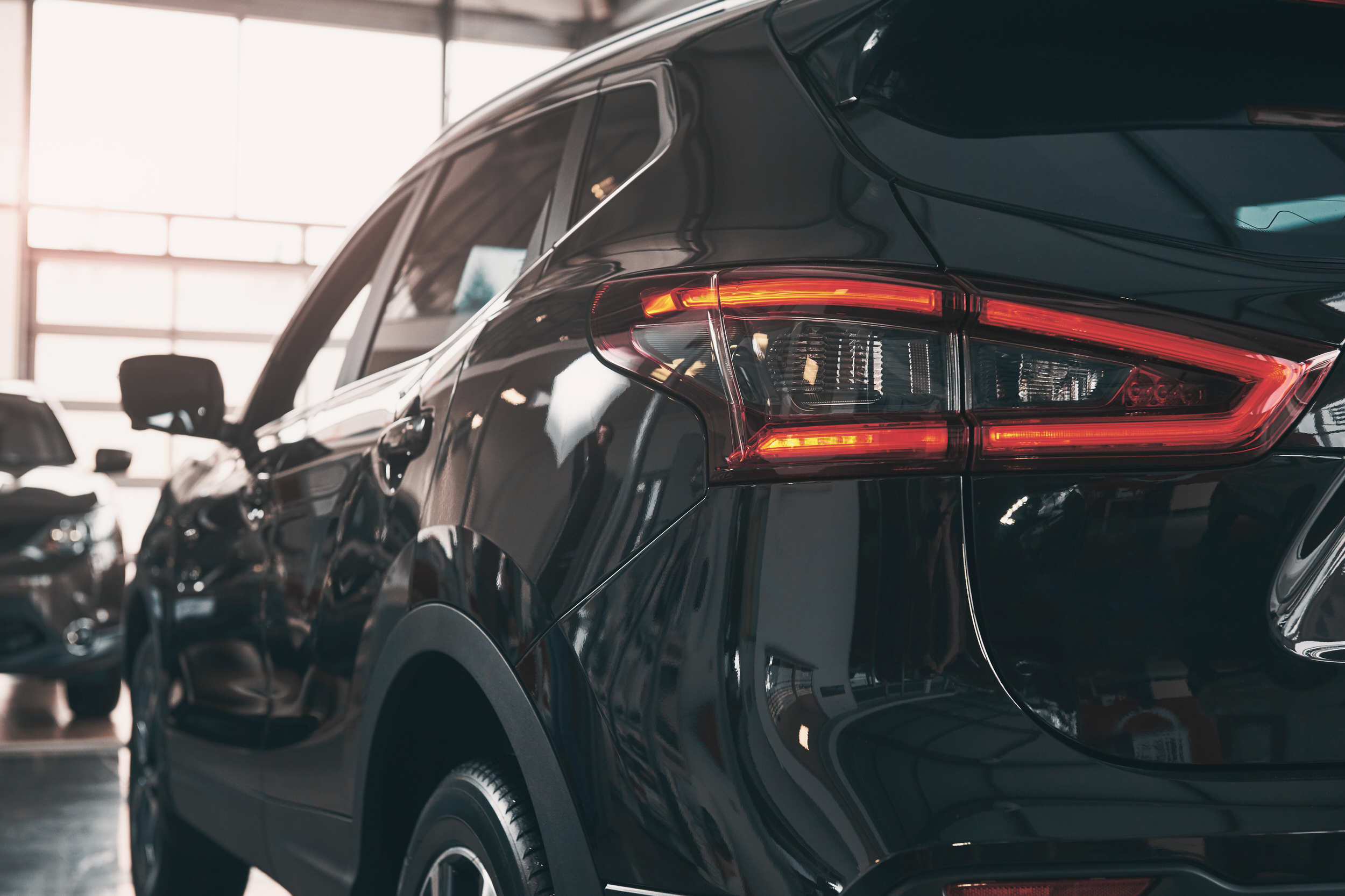 Close-up of the rear end of a black SUV inside a car dealership, showing taillights and part of the side mirror.