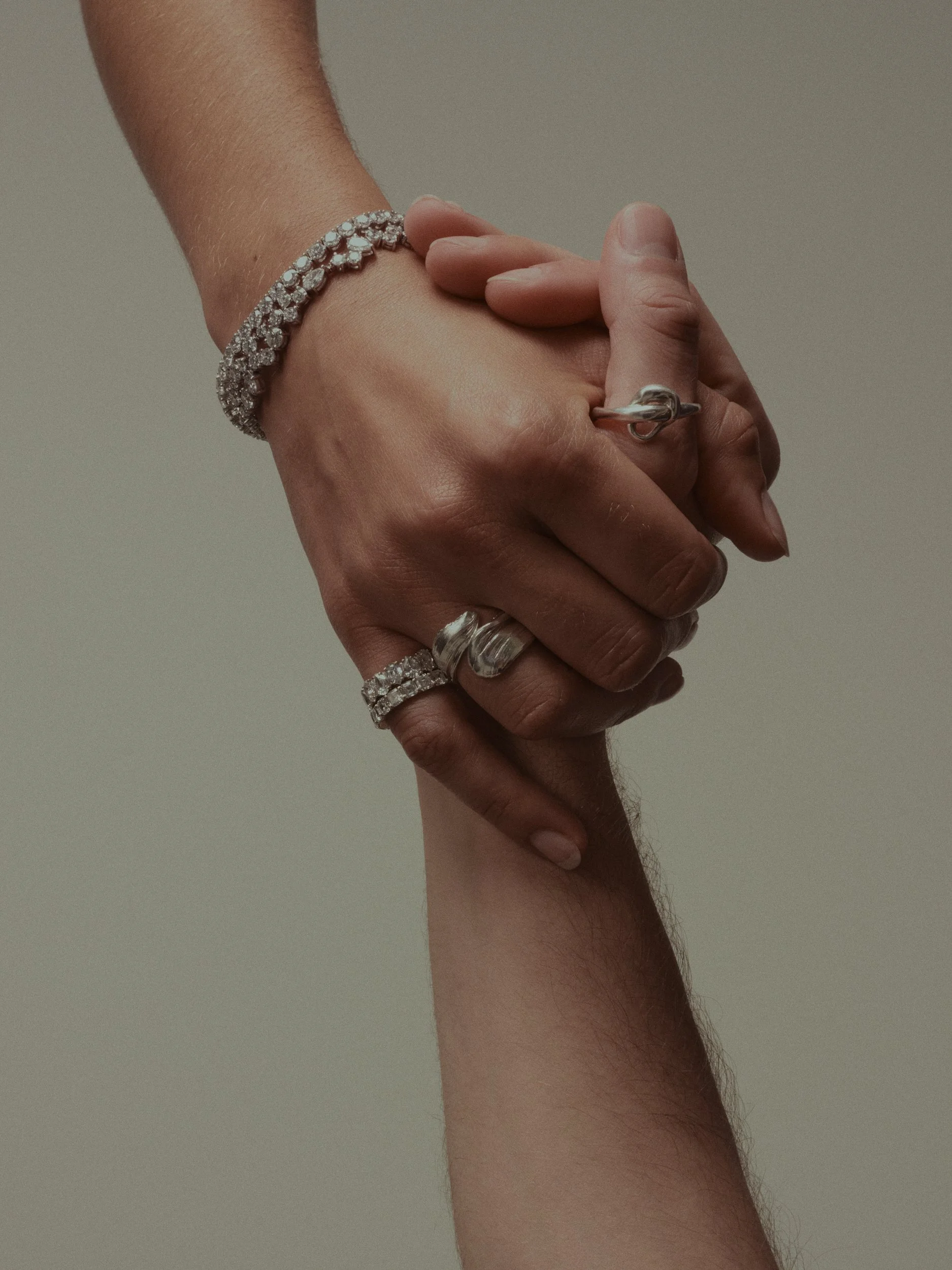 Zwei Hände halten sich ineinander, die Hand mit mehreren silbernen Ringen und Armbändern. Die Bilder sind Nahaufnahmen.
