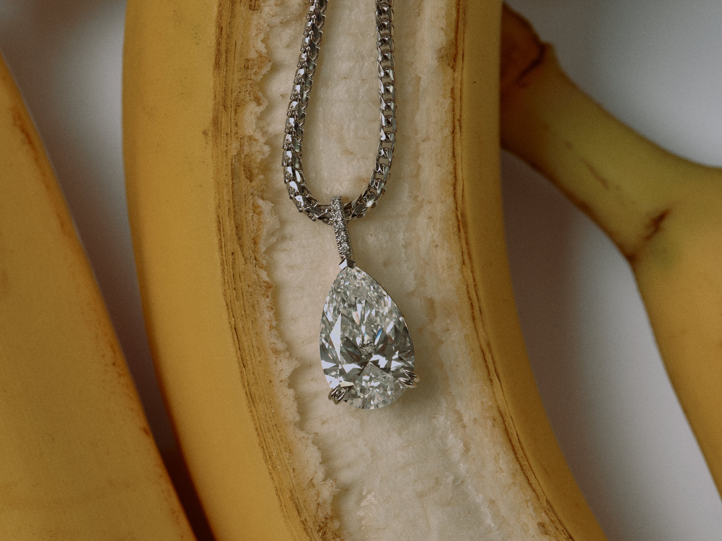 Ein silberne Halskette mit einem großen diamantähnlichen Anhänger liegt auf einer gelben Banane.