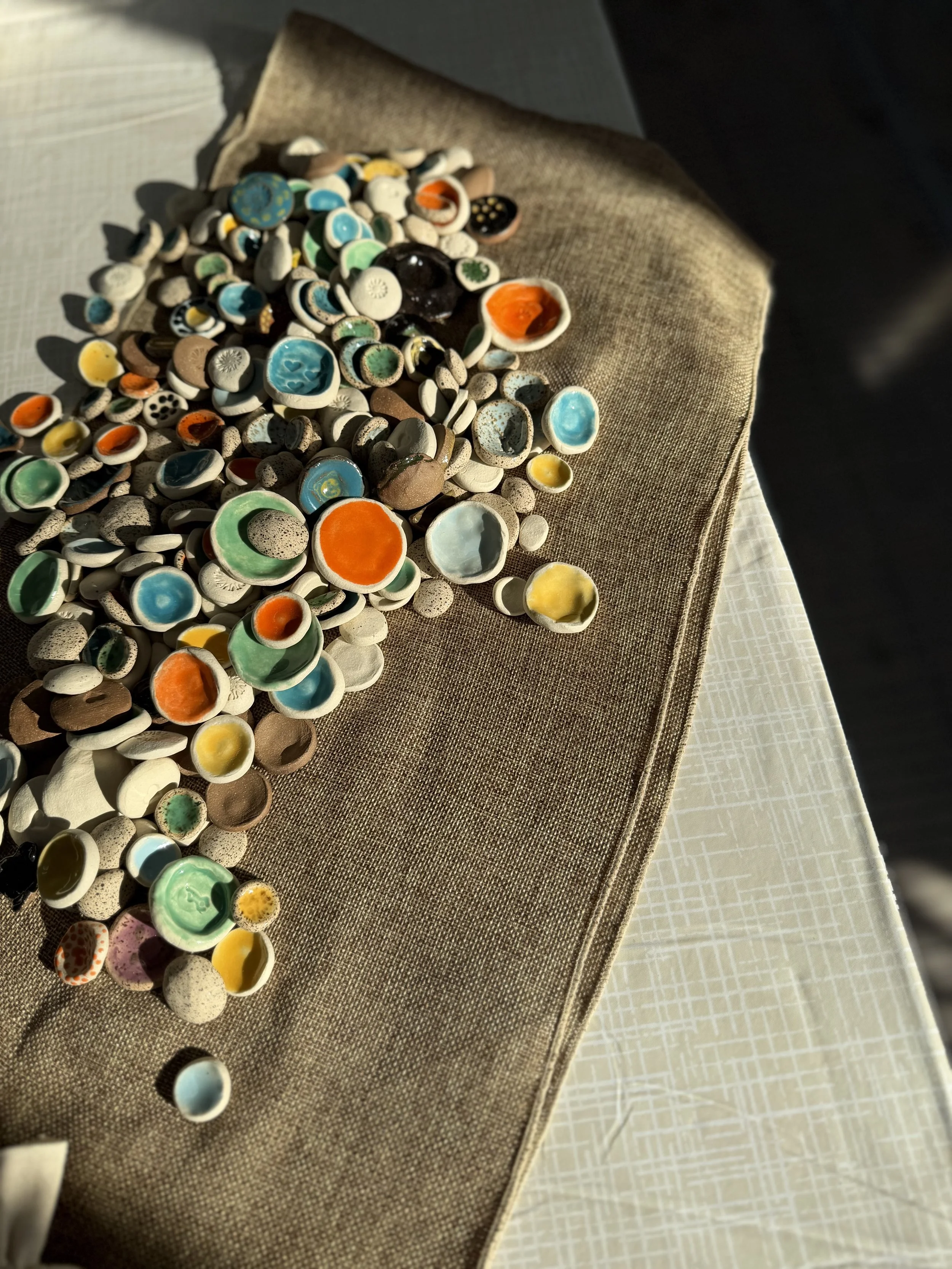 A collection of small, colorful ceramic or glass bowl like objects scattered on a fabric surface with a textured tablecloth underneath.