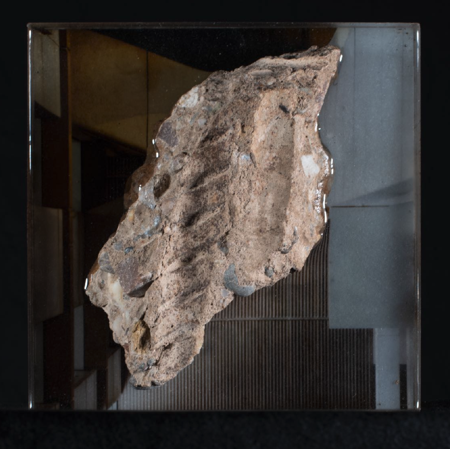 A colour image of what appears to be a piece of rock or concrete hanging in space with wall tiling behind.