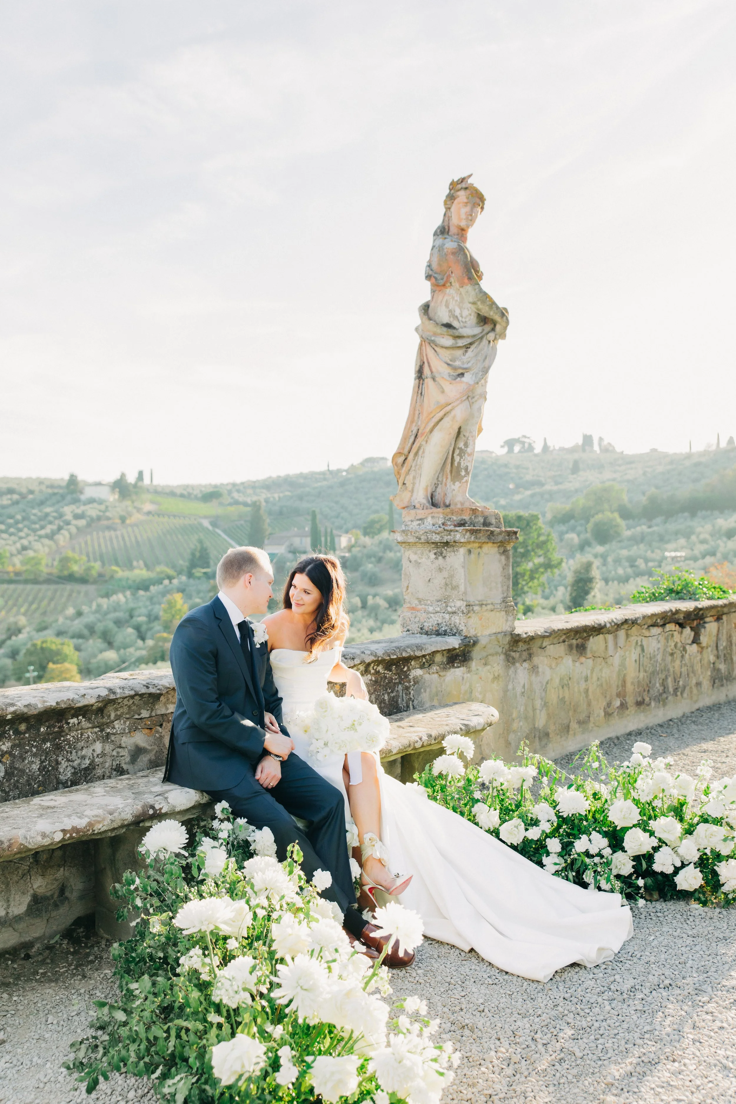 Elegant dining hall with a long table decorated with white flowers, glassware, and candles, set against a backdrop of ornate, painted walls and arched ceilings with sculptures.