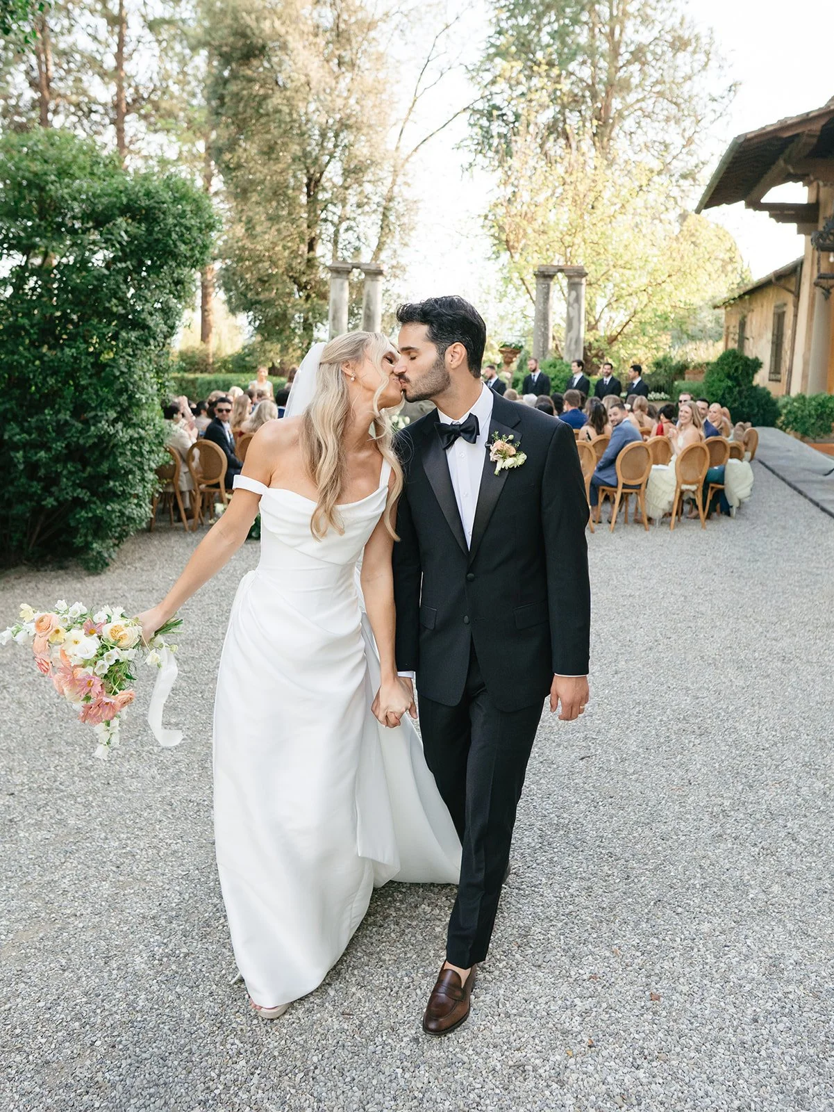 Bride and groom holding hands and sharing a kiss at an outdoor wedding ceremony.
