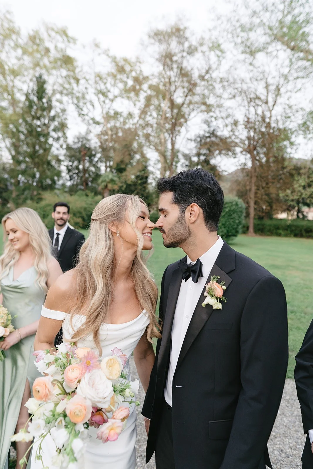 Bride and groom sharing an intimate moment at their wedding, outdoors with bridesmaids and groomsmen in the background.