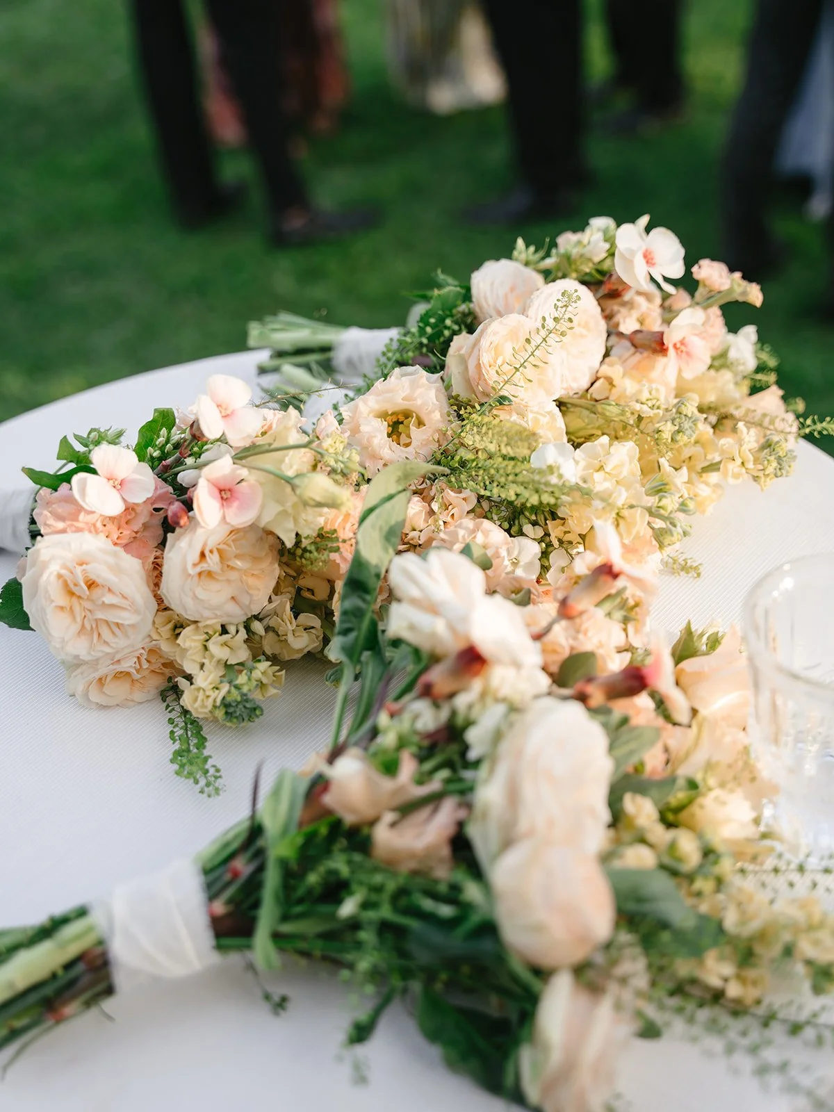 A bouquet of pale peach and white flowers, including roses, on a white tablecloth at an outdoor event.