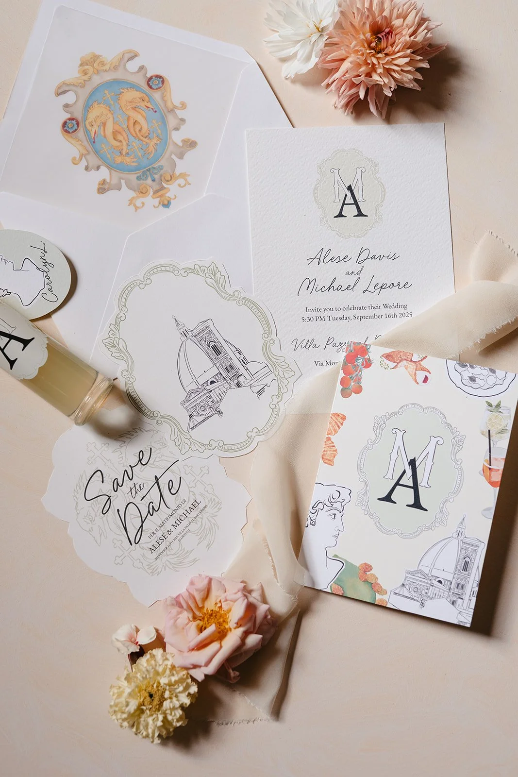 Wedding invitation suite with monogram, save the date card, and additional stationery, decorated with flowers and illustrations of a church and cityscape, on a light-colored surface.