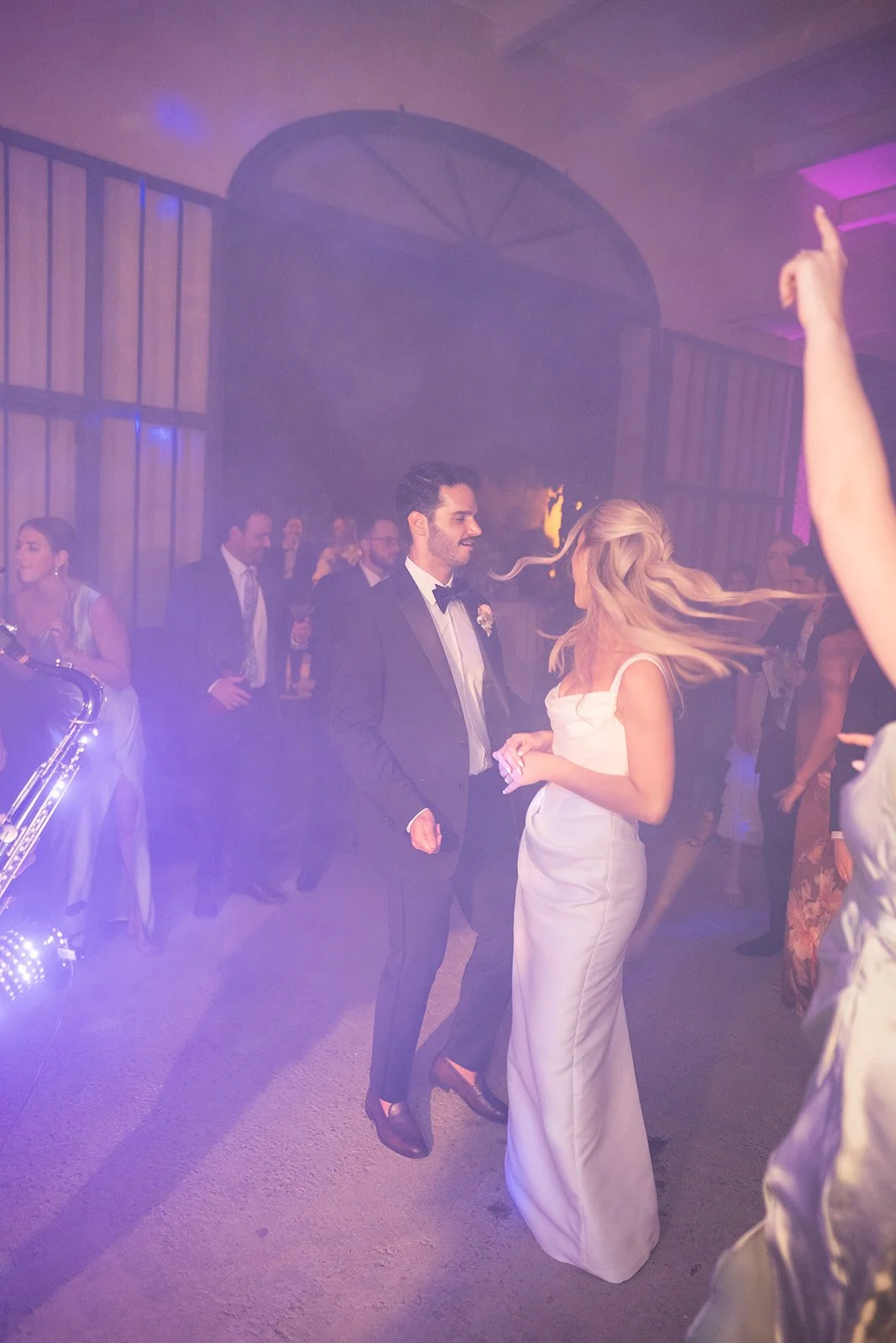 A bride and groom dancing at a wedding reception with guests watching in the background.