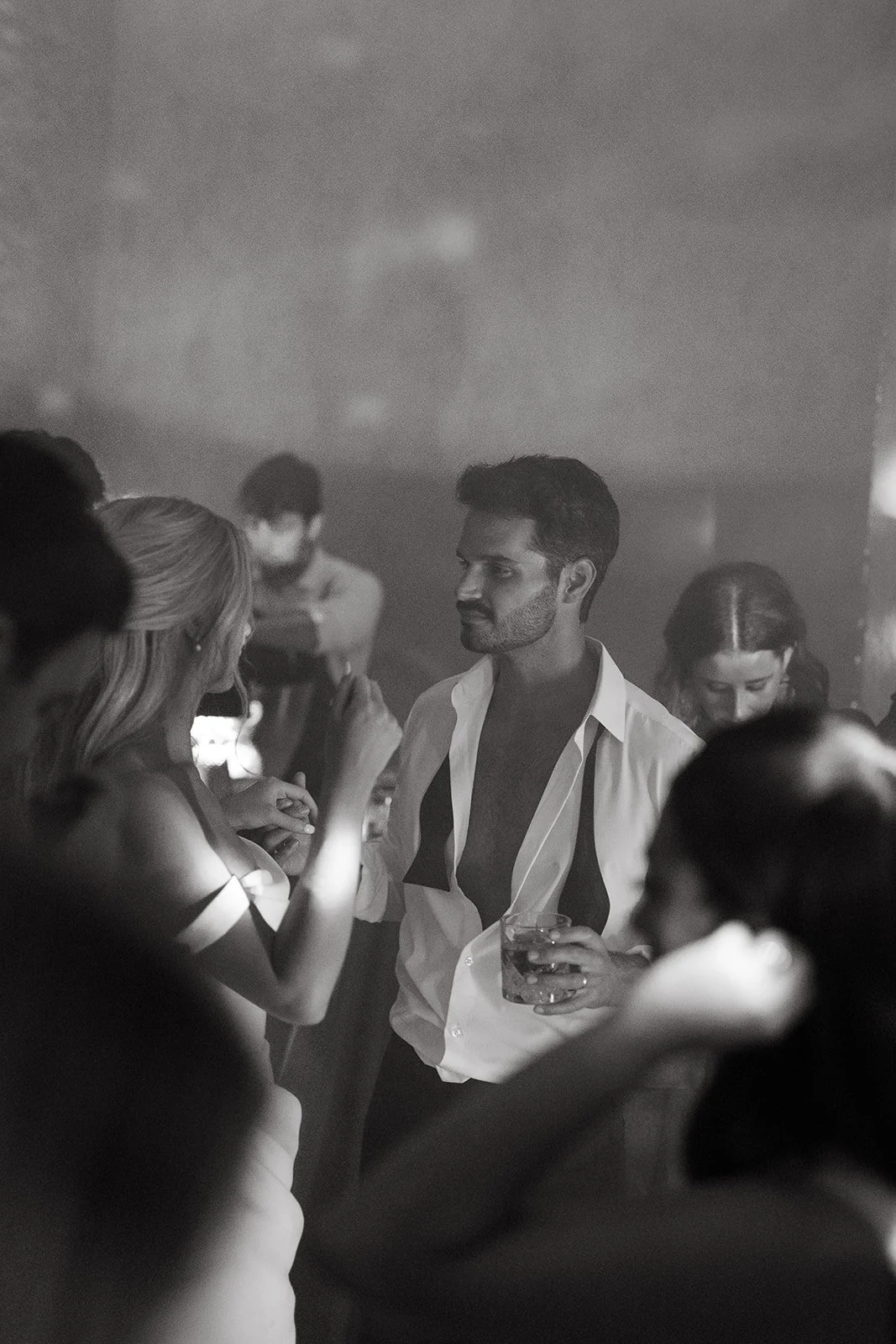 People socializing at a party with a man holding a drink in a bar, black and white photograph.