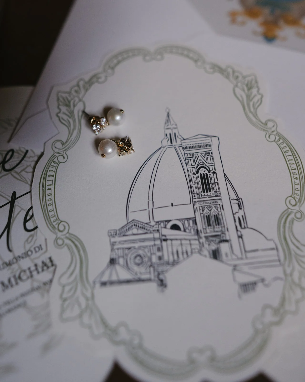 Earrings with pearls and rhinestones placed on a black and white illustration of a cathedral with a decorative border.